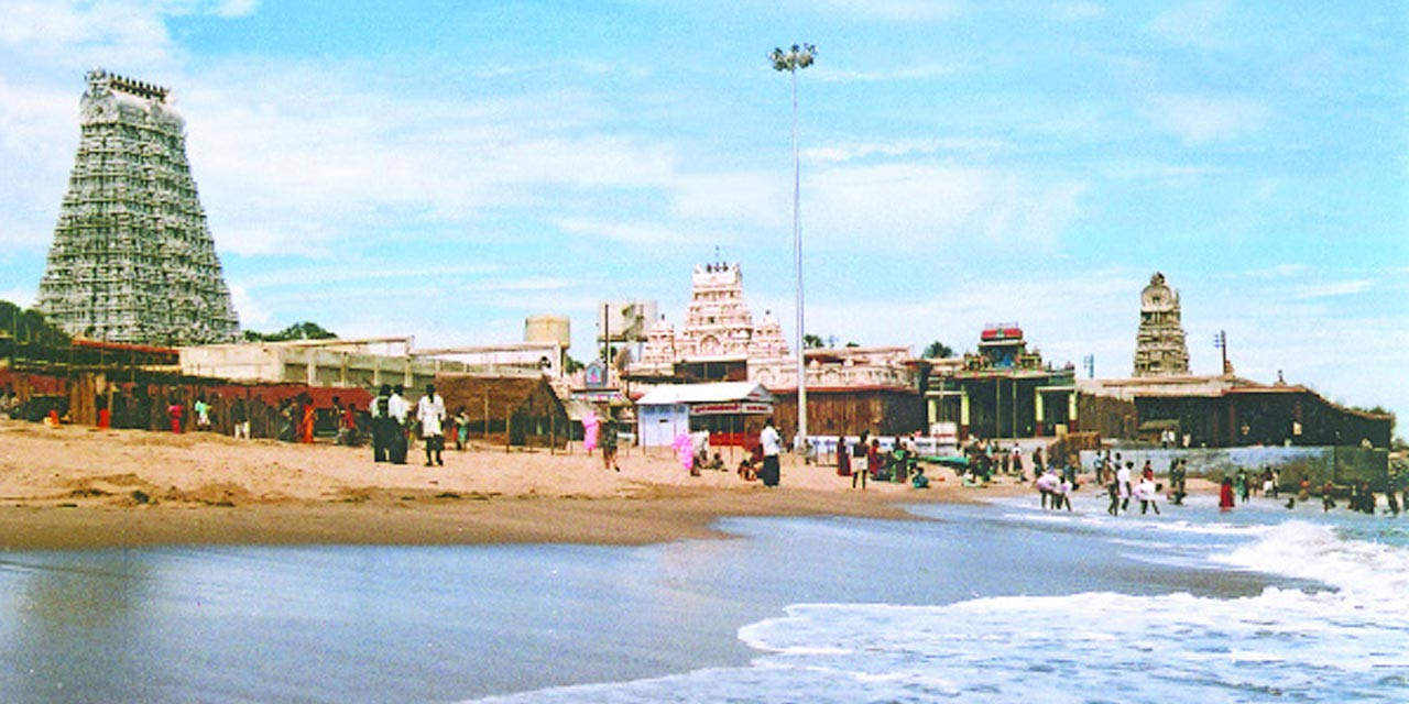 Hindu Temple 桌布 壁紙 — 熱鬧的海濱寺廟建築群，高聳的哥普蘭（gopurams）和人們在明亮的藍天下沿著海岸線漫步。