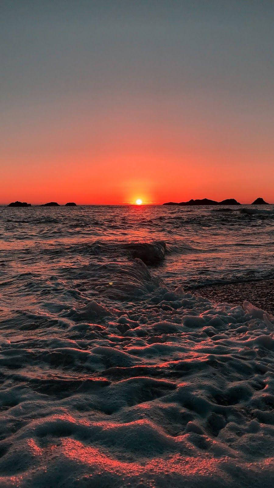 Aesthetic Sunset 桌布 壁紙 — 熾熱的夕陽以鮮豔的橙色和紅色色調描繪了海浪和遙遠的島嶼。