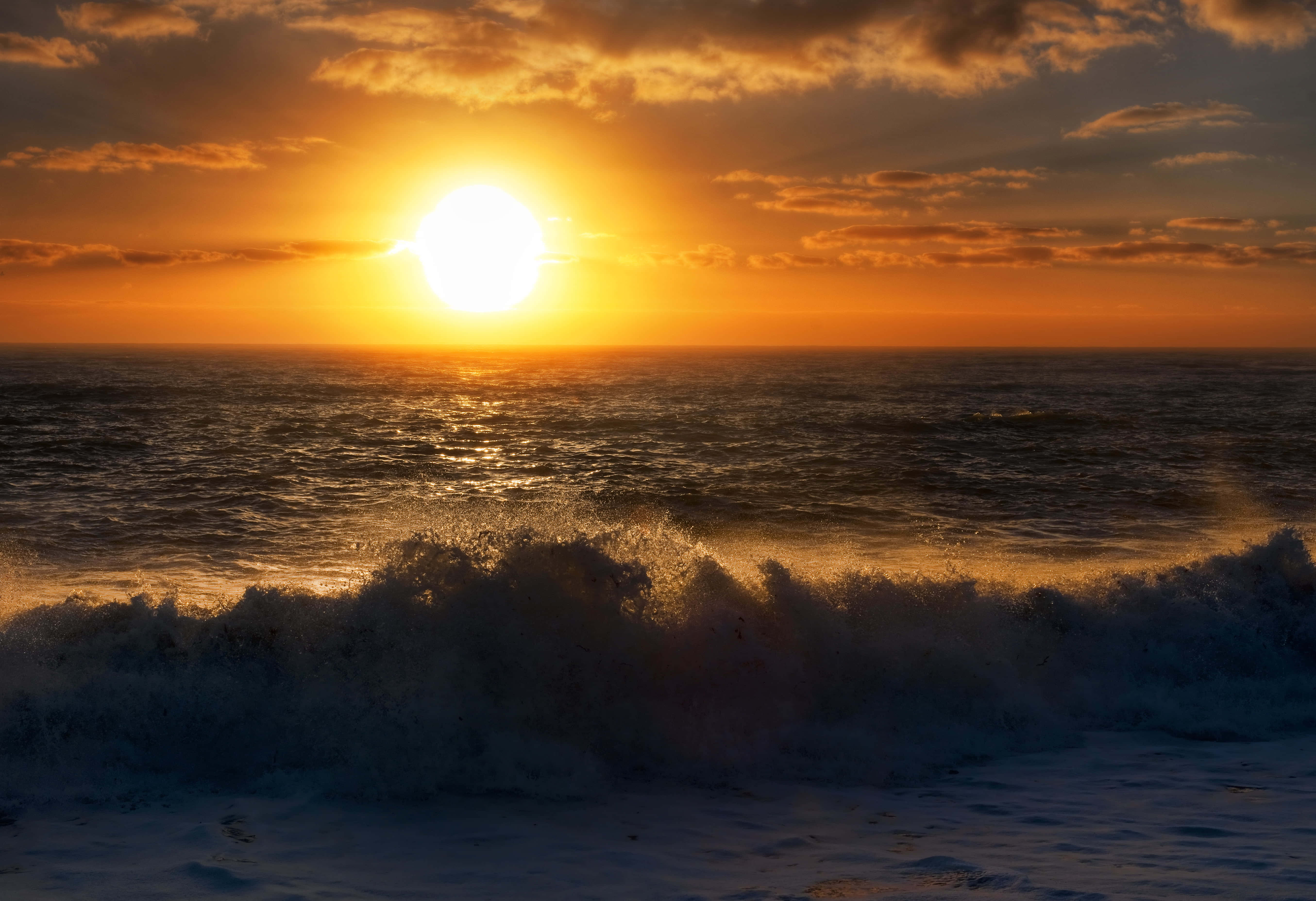 Beach Waves 桌布 壁紙 — 熾熱的夕陽在戲劇性的多雲天空背景下，將金色光芒投射在洶湧的海浪上。