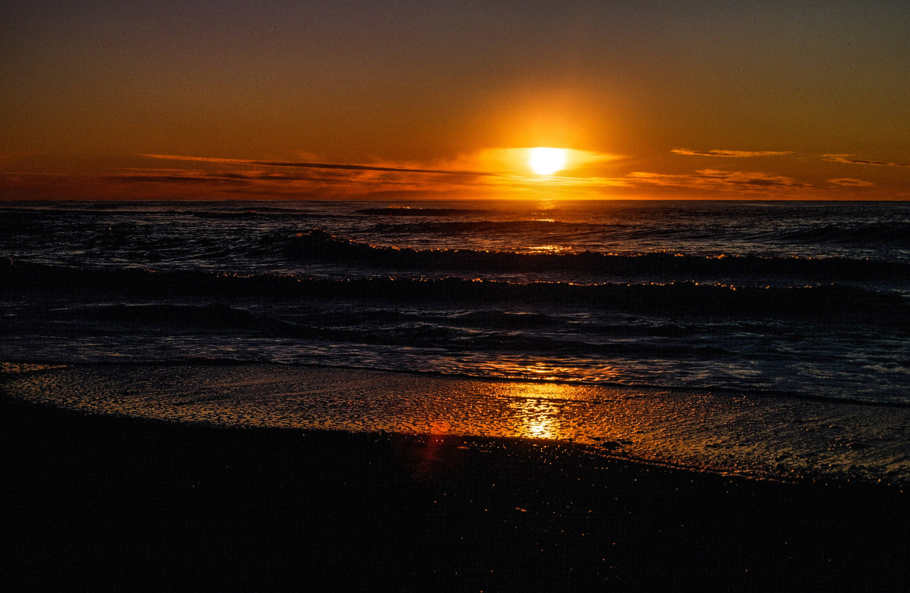 俄勒岡州 桌布 壁紙 — 熾熱的夕陽在海面上閃耀，海浪拍打著深色沙灘。