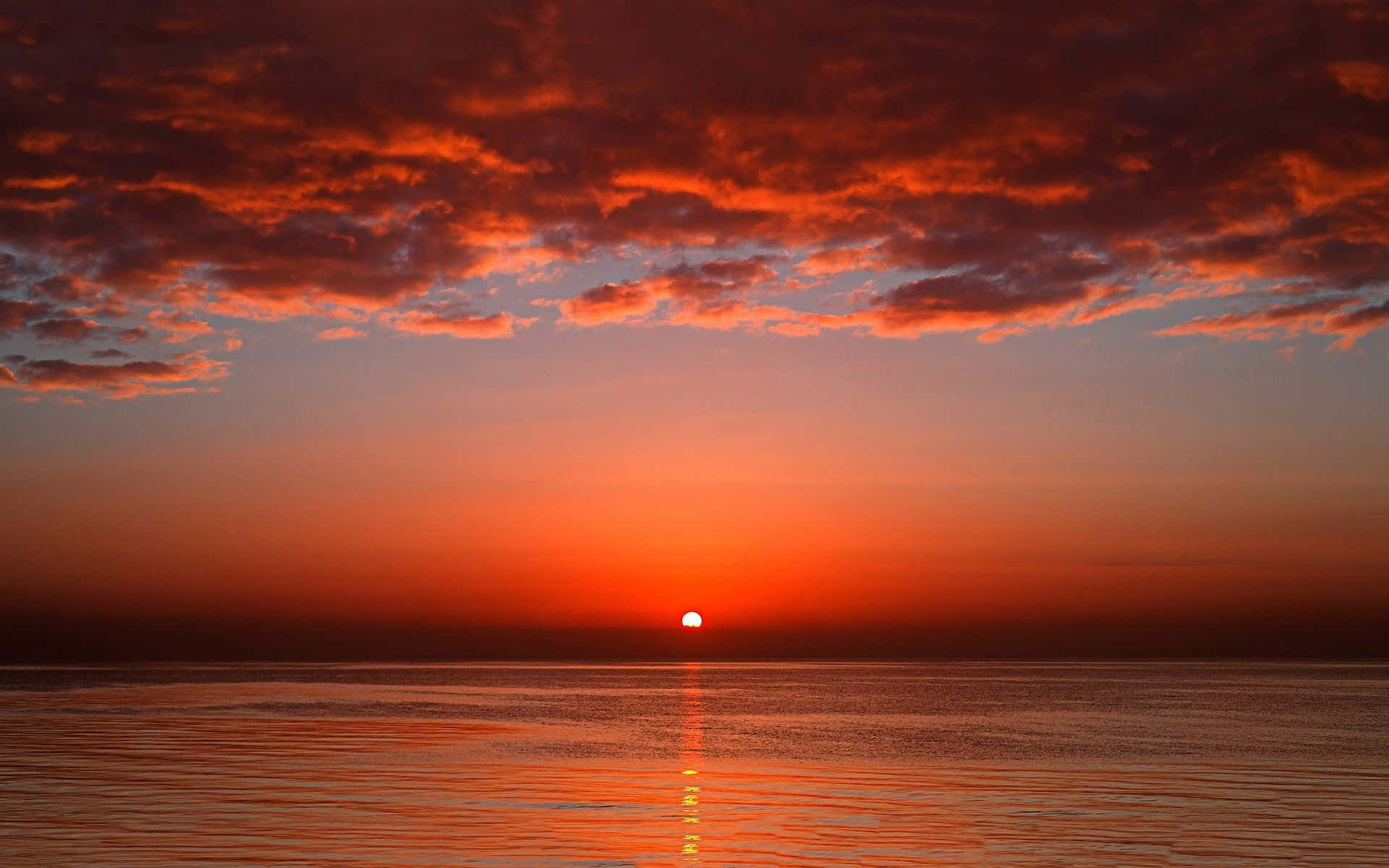 海洋 桌布 壁紙 — 熾熱的夕陽將天空和寧靜的水面染成鮮豔的橙色和紅色色調，太陽沉入地平線以下。