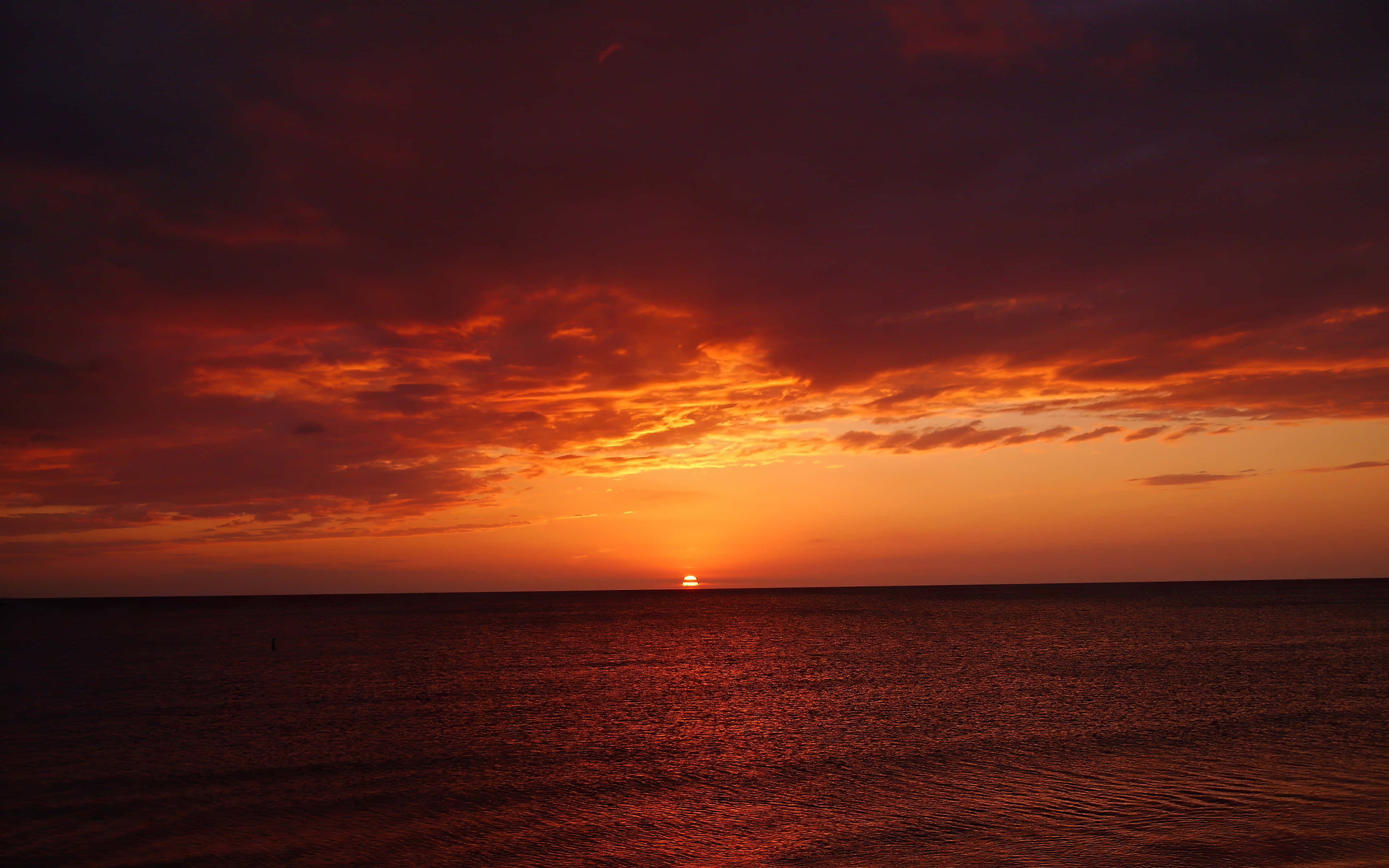 Beautiful Sky 桌布 壁紙 — 熾熱的夕陽將天空和海洋染成深紅和橙色，太陽沉入地平線以下。