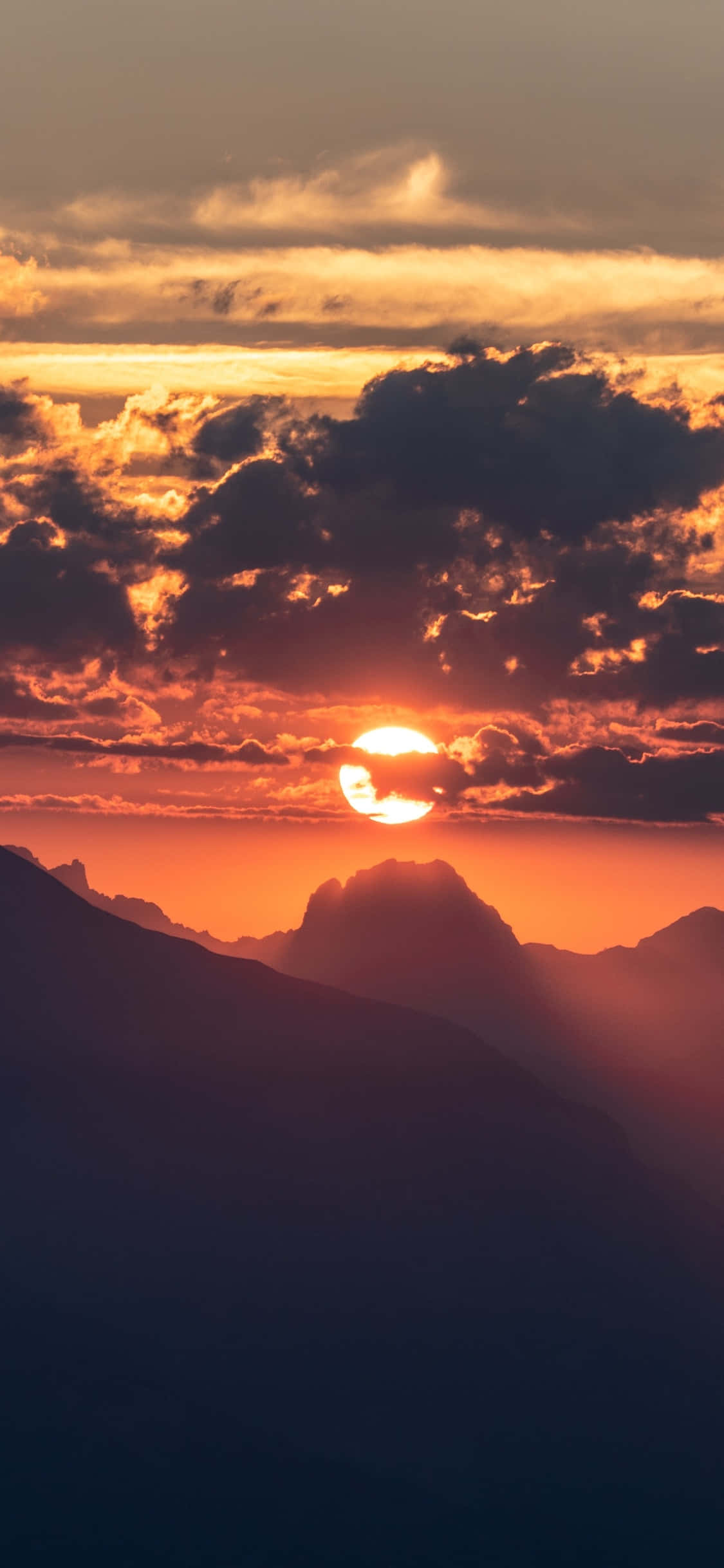 Sunrise iPhone 桌布 壁紙 — 熾熱的夕陽將天空染成橙色和紅色，太陽在戲劇性的雲層後方落在山頂之後。