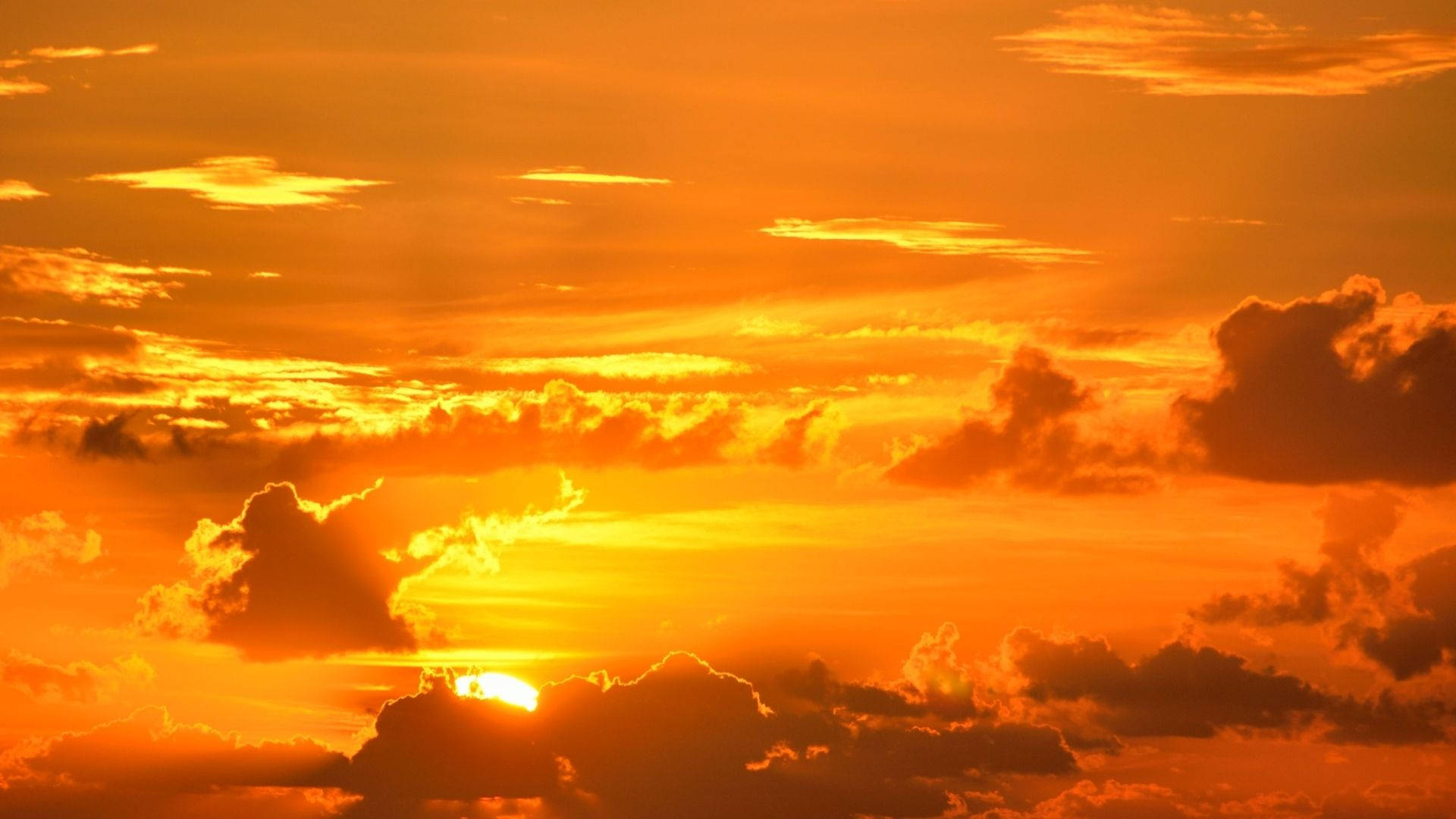 Orange 桌布 壁紙 — 熾熱的夕陽將天空染成鮮豔的橙色和金色，雲朵發光並在夕陽下形成剪影。