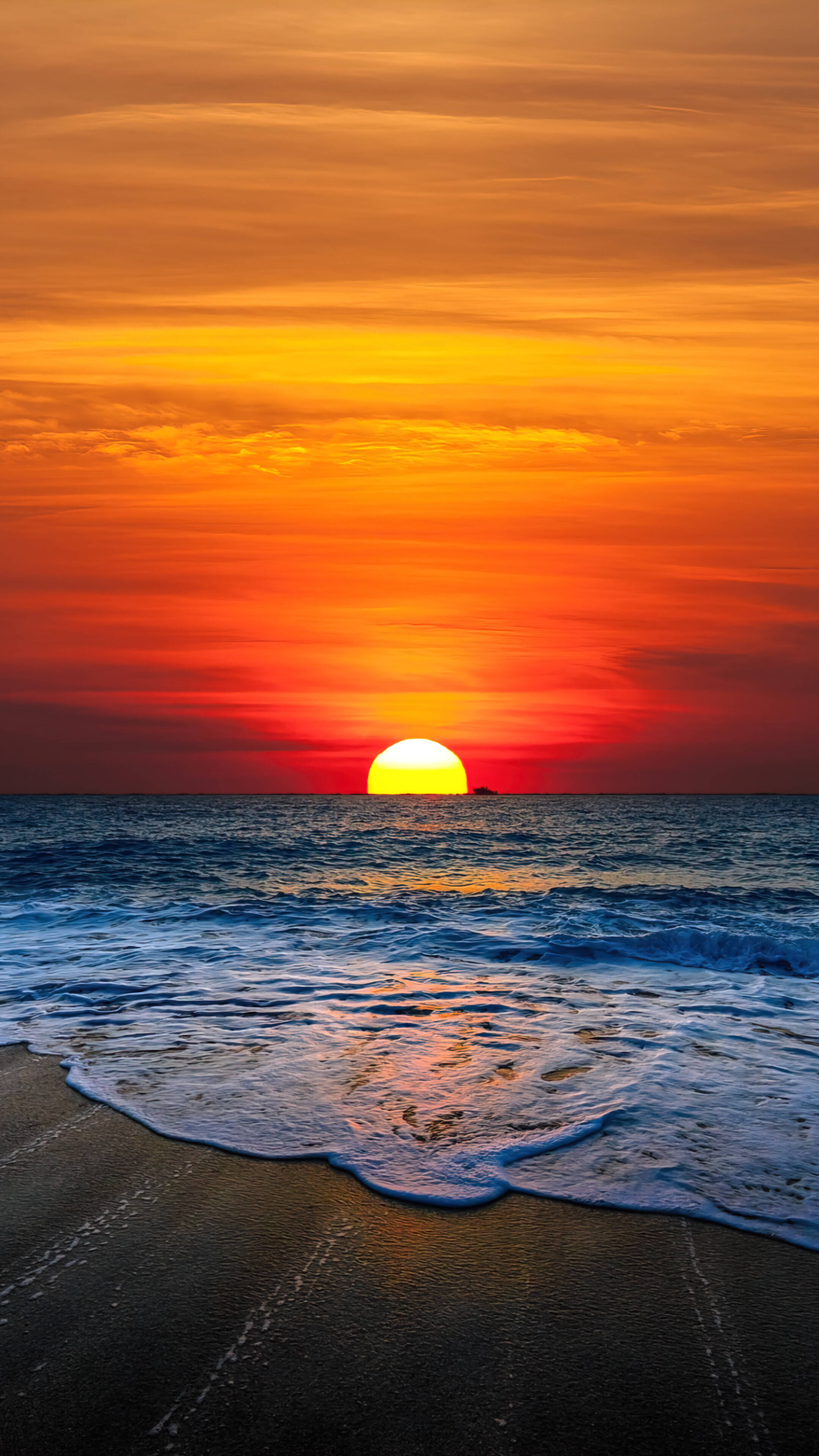 日落 桌布 壁紙 — 熾熱的夕陽將天空染成鮮豔的橙色和紅色，海浪拍打著深色的沙灘。