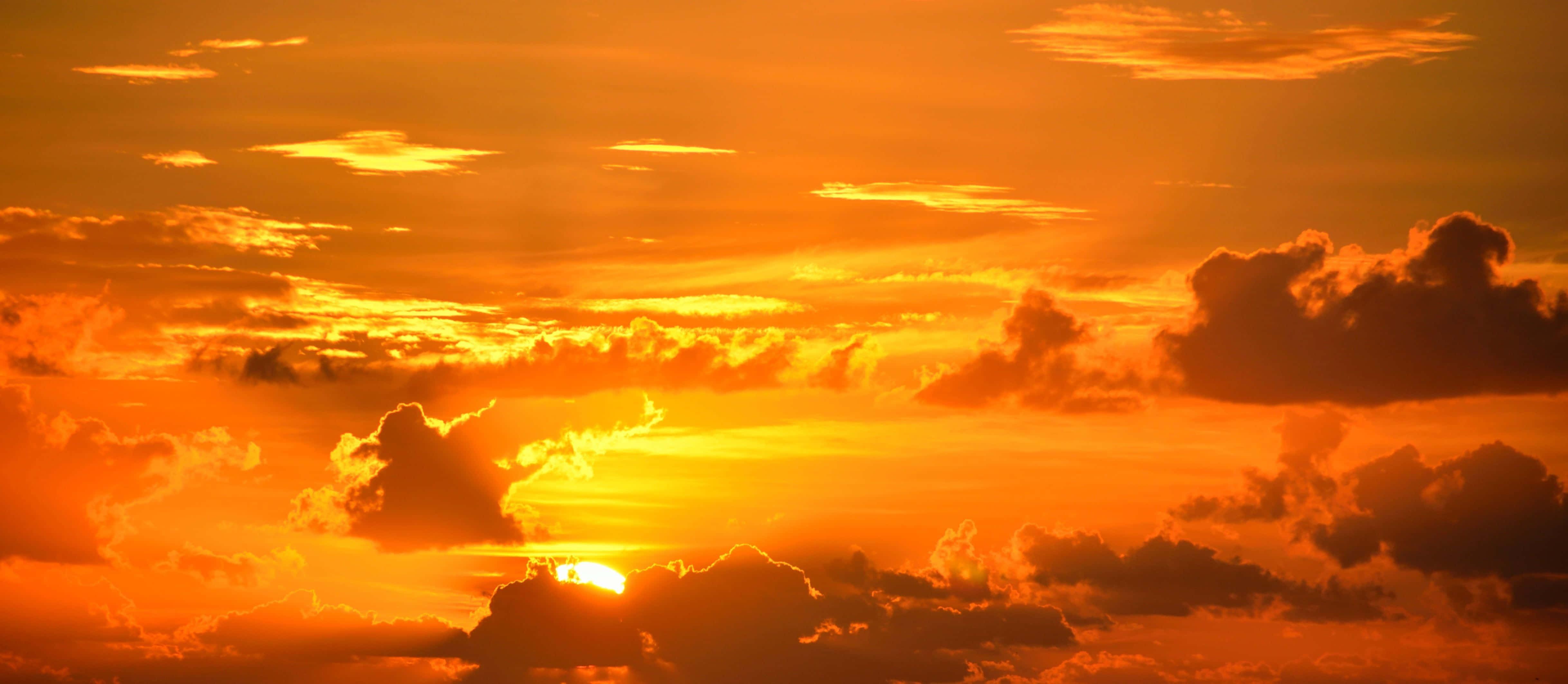 Yellow Sunset 桌布 壁紙 — 熾熱的夕陽將天空染成鮮豔的橙色和紅色，太陽在戲劇性的雲層後落下。