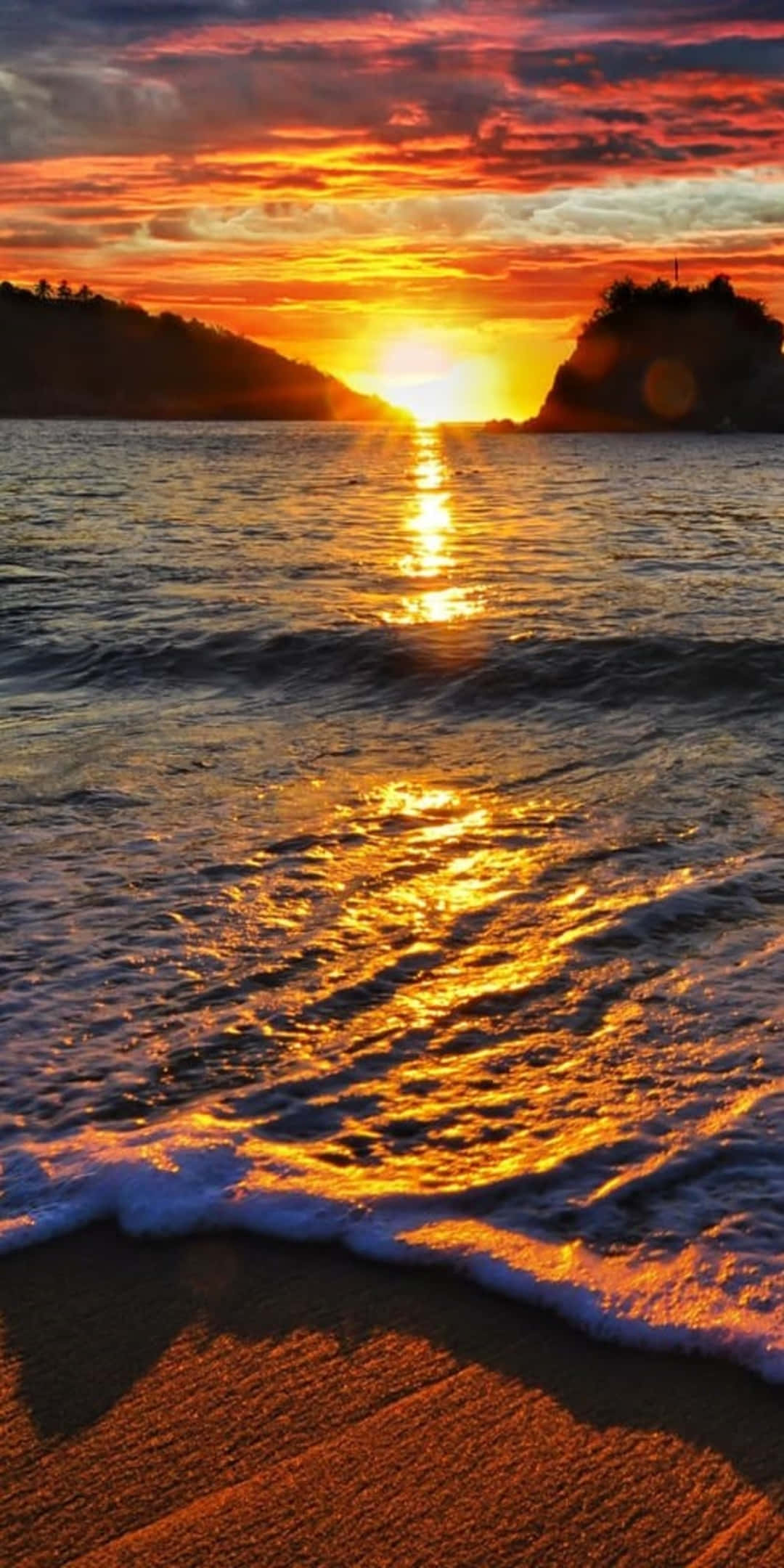Pixel 3 Beach 桌布 壁紙 — 熾熱的夕陽將海洋染成金色和橙色，海浪拍打著沙灘，兩側是剪影般的懸崖。