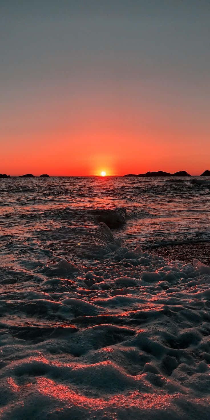 Big 桌布 壁紙 — 熾熱的夕陽將海洋染成鮮豔的橙色，海浪拍打岩石海岸，遠處的島嶼在發光的地平線上形成剪影。