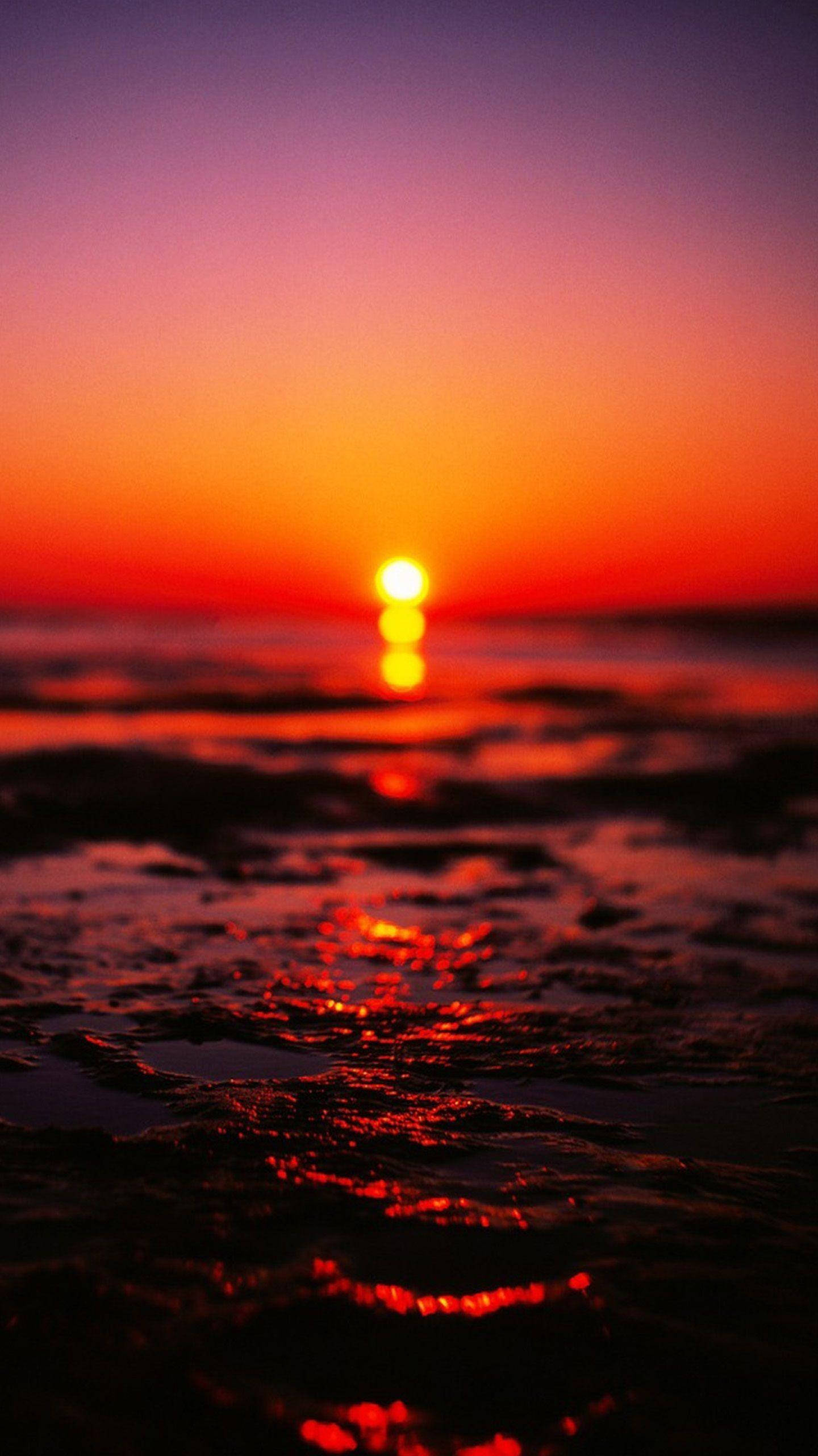 Sunset iPhone 桌布 壁紙 — 熾熱的夕陽將海洋染成鮮豔的橙色和紫色，太陽沉入地平線下。