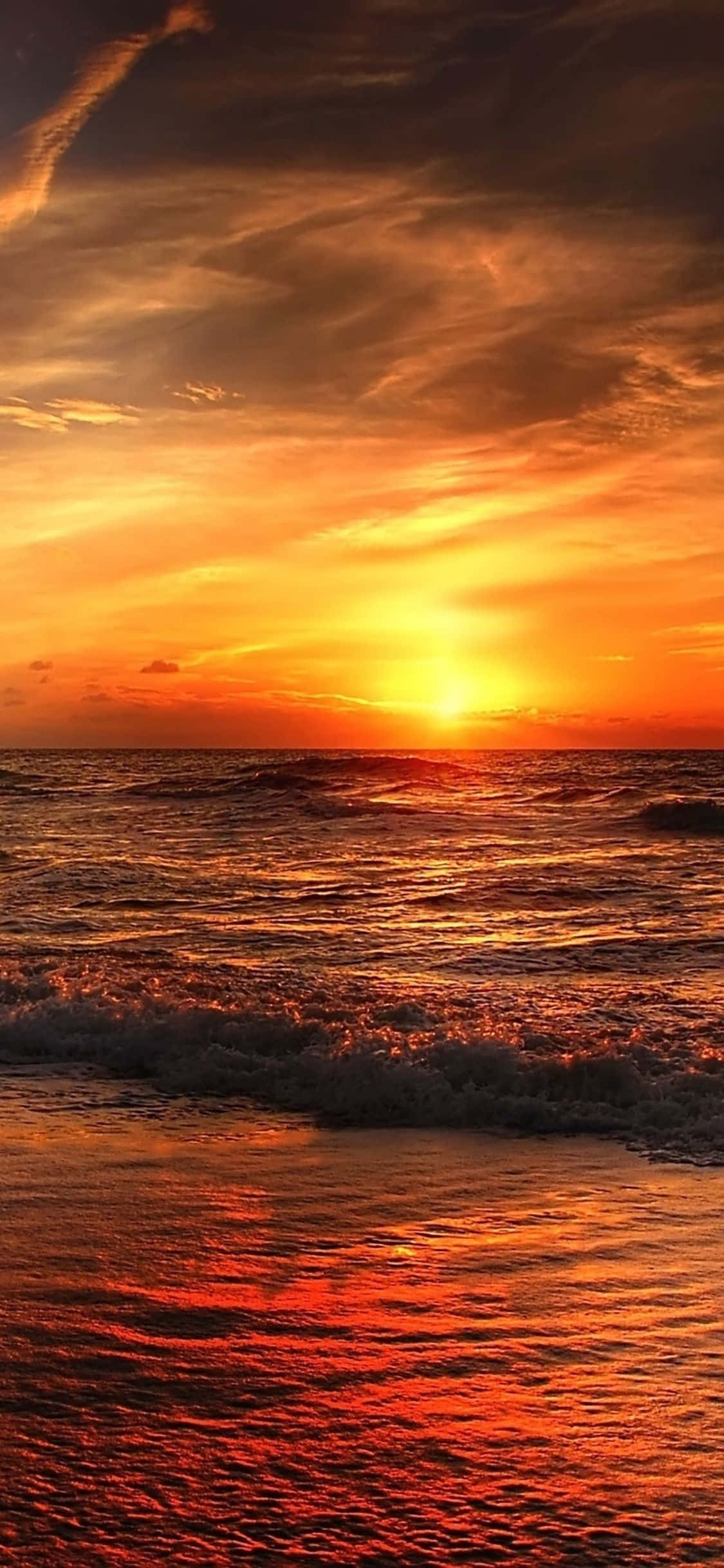 Sunset Beach iPhone 桌布 壁紙 — 熾熱的夕陽將海洋染成鮮豔的橙色和紅色，海浪拍打著濕漉漉的沙灘。