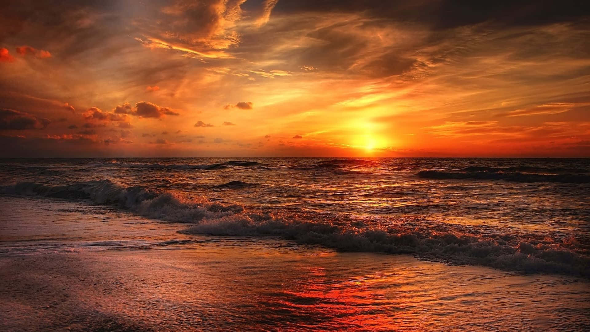Sunset Photography 桌布 壁紙 — 熾熱的夕陽將海洋染成鮮豔的橙色和紅色，海浪在戲劇性的雲層下拍打著沙灘。