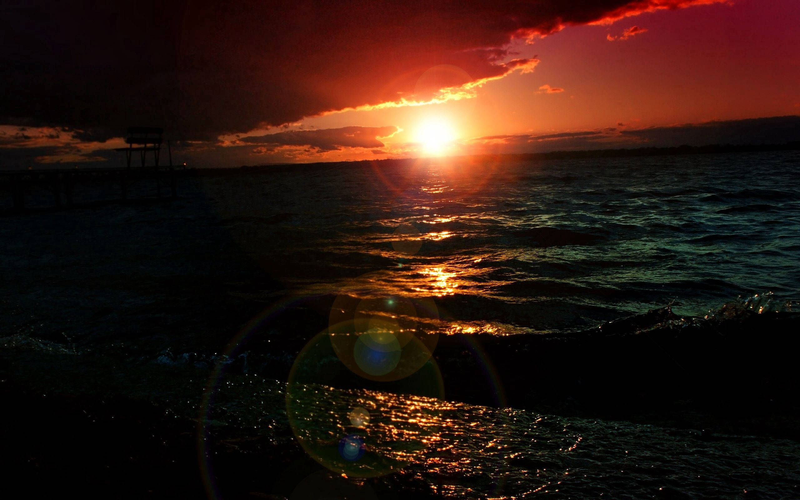 Very Pretty 桌布 壁紙 — 熾熱的夕陽將金色光芒投射在洶湧的海浪上，前景有碼頭剪影和鏡頭光暈。