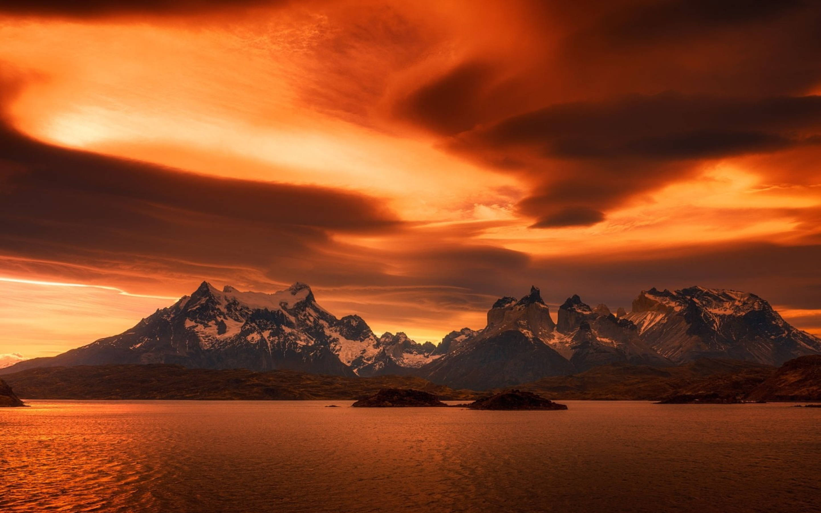 Patagonia 桌布 壁紙 — 熾熱的橙色夕陽在平靜的湖面上映照出溫暖的光芒，照耀著積雪覆蓋的山脈。