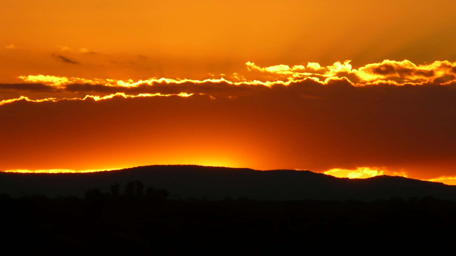 橙色夕陽，雲朵在黑暗山丘上發光 — 橘色美學 GIF 壁紙