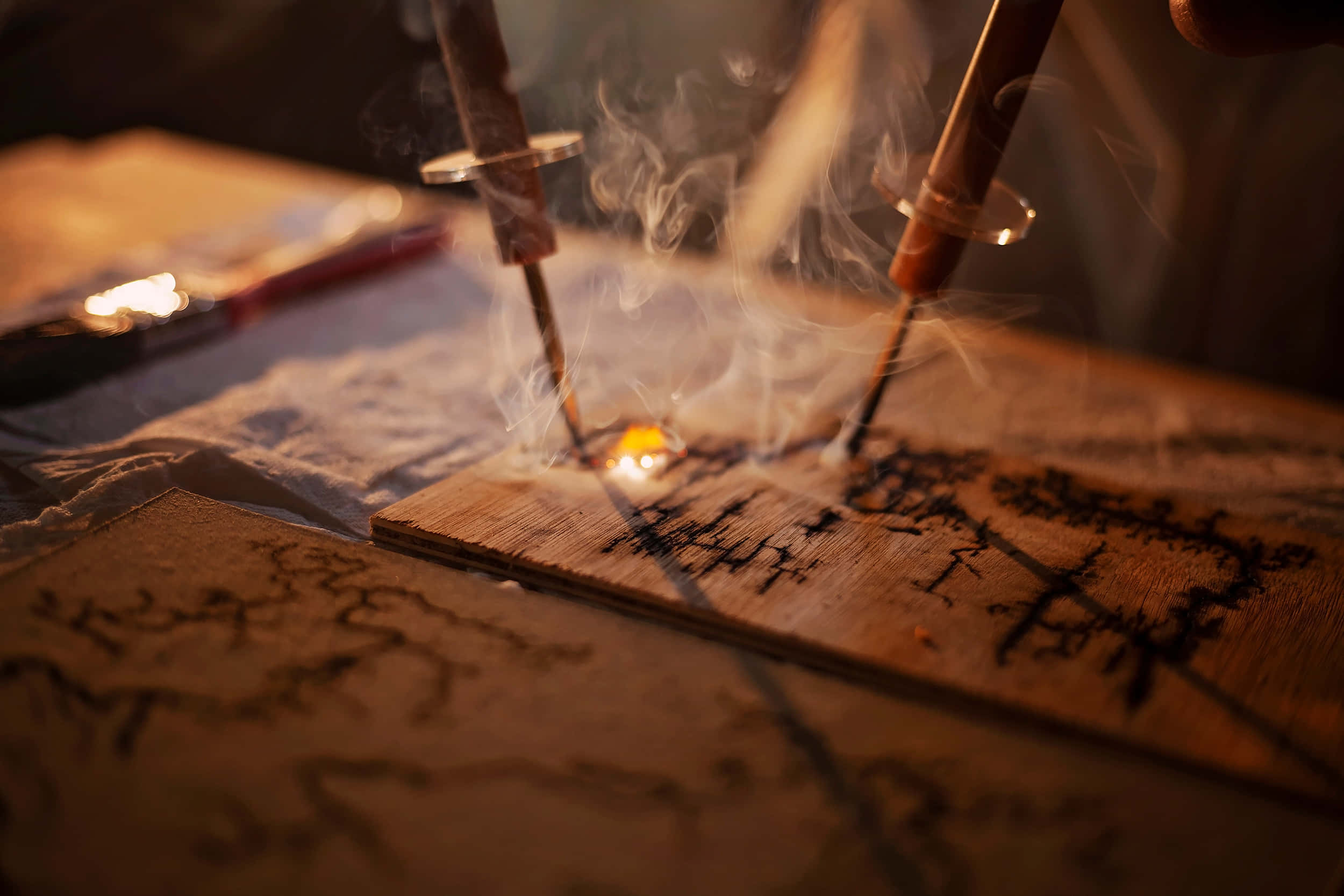 Wood Burning 桌布 壁紙 — 燃燒中的香枝在木質表面上冒煙的特寫，溫暖的金色光線和柔和的煙霧繚繞。