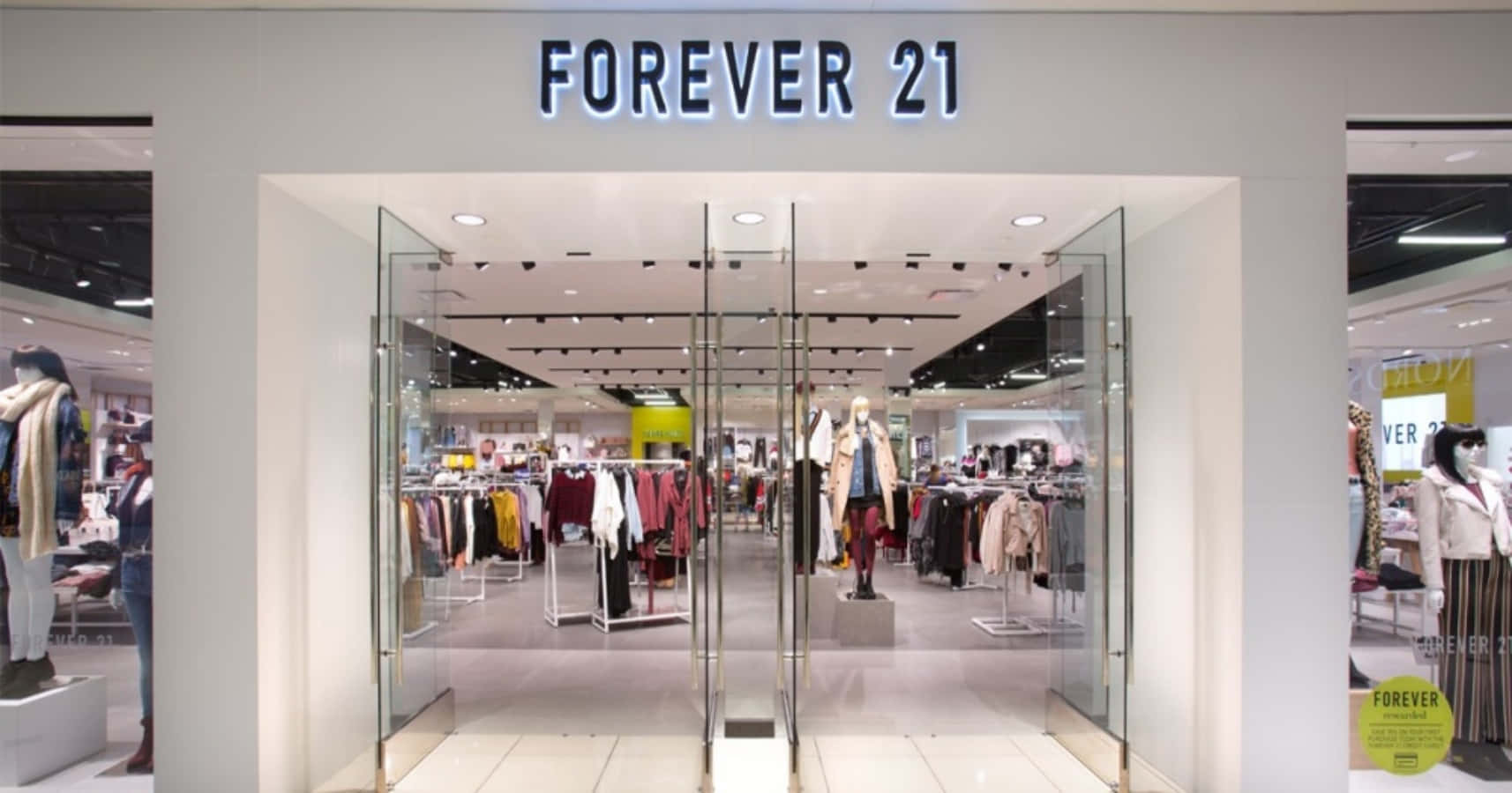 永遠21 桌布 壁紙 — 燈光明亮的Forever 21商店入口，玻璃門內展示著色彩繽紛的衣物架和模特兒。