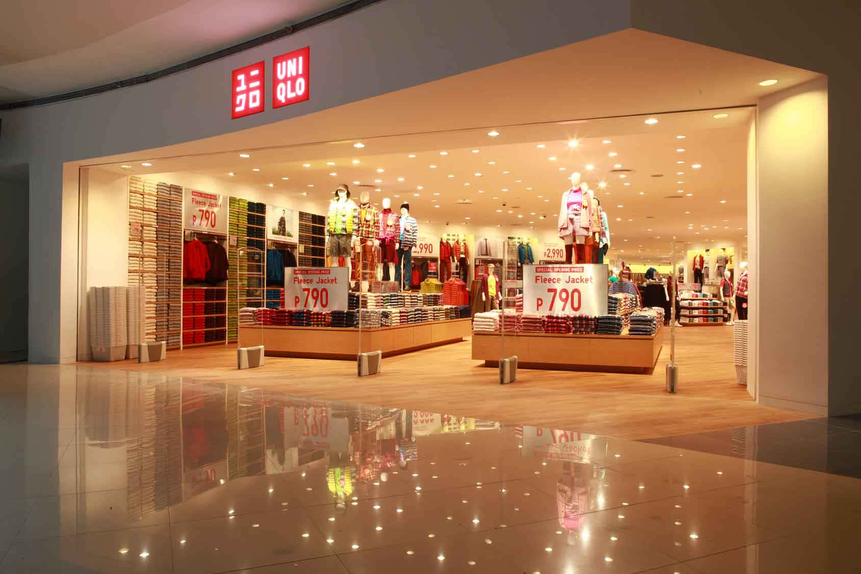 Uniqlo 桌布 壁紙 — 燈光明亮的Uniqlo店鋪入口，人體模型和價格標籤映照在拋光地磚上。