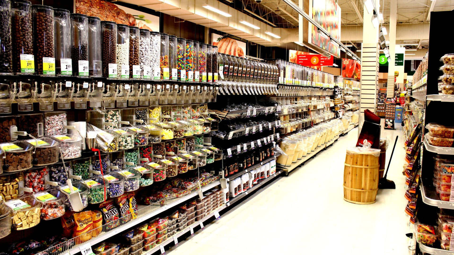 Shop 桌布 壁紙 — 燈光明亮的雜貨店通道，透明容器和貨架上擺滿了色彩繽紛的散裝糖果和零食。