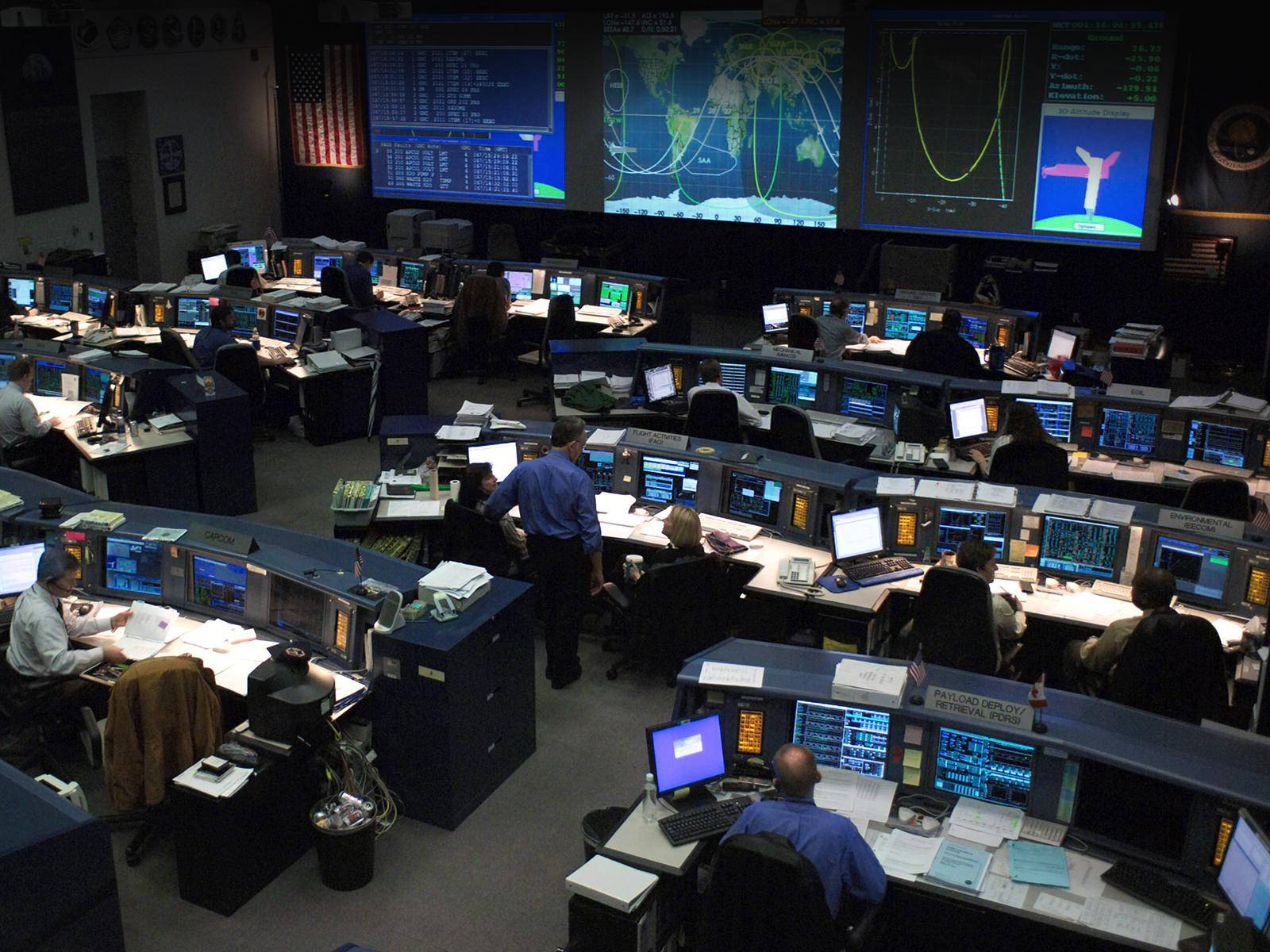 NASA 動態圖片 桌布 壁紙 — 燈光昏暗的NASA任務控制室，工程師們在電腦工作站前監控大螢幕上的全球數據。
