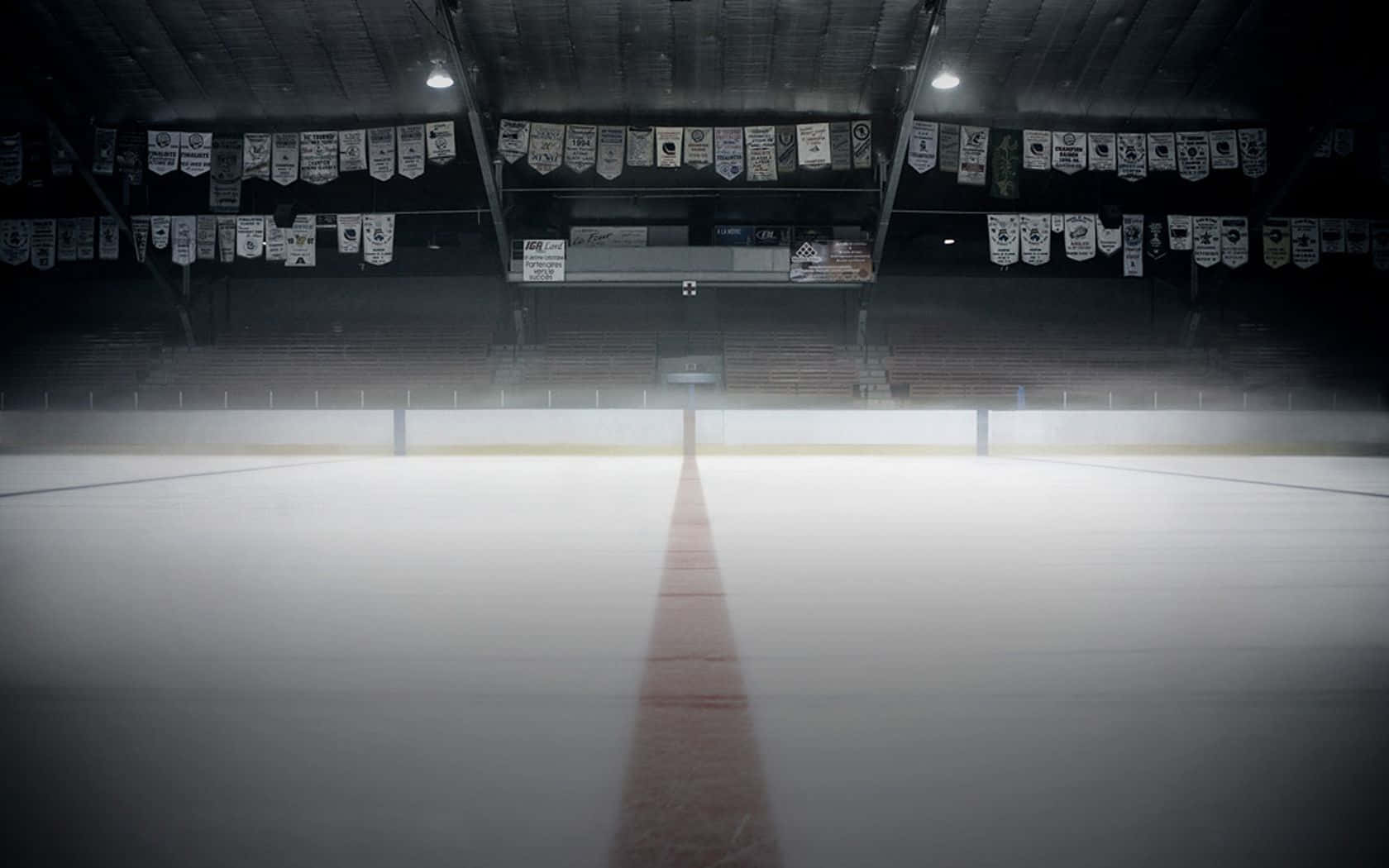 Ice Rink 桌布 壁紙 — 燈光昏暗的冰球場，紅色中線延伸至空蕩蕩的看台，看台上裝飾著冠軍旗幟。