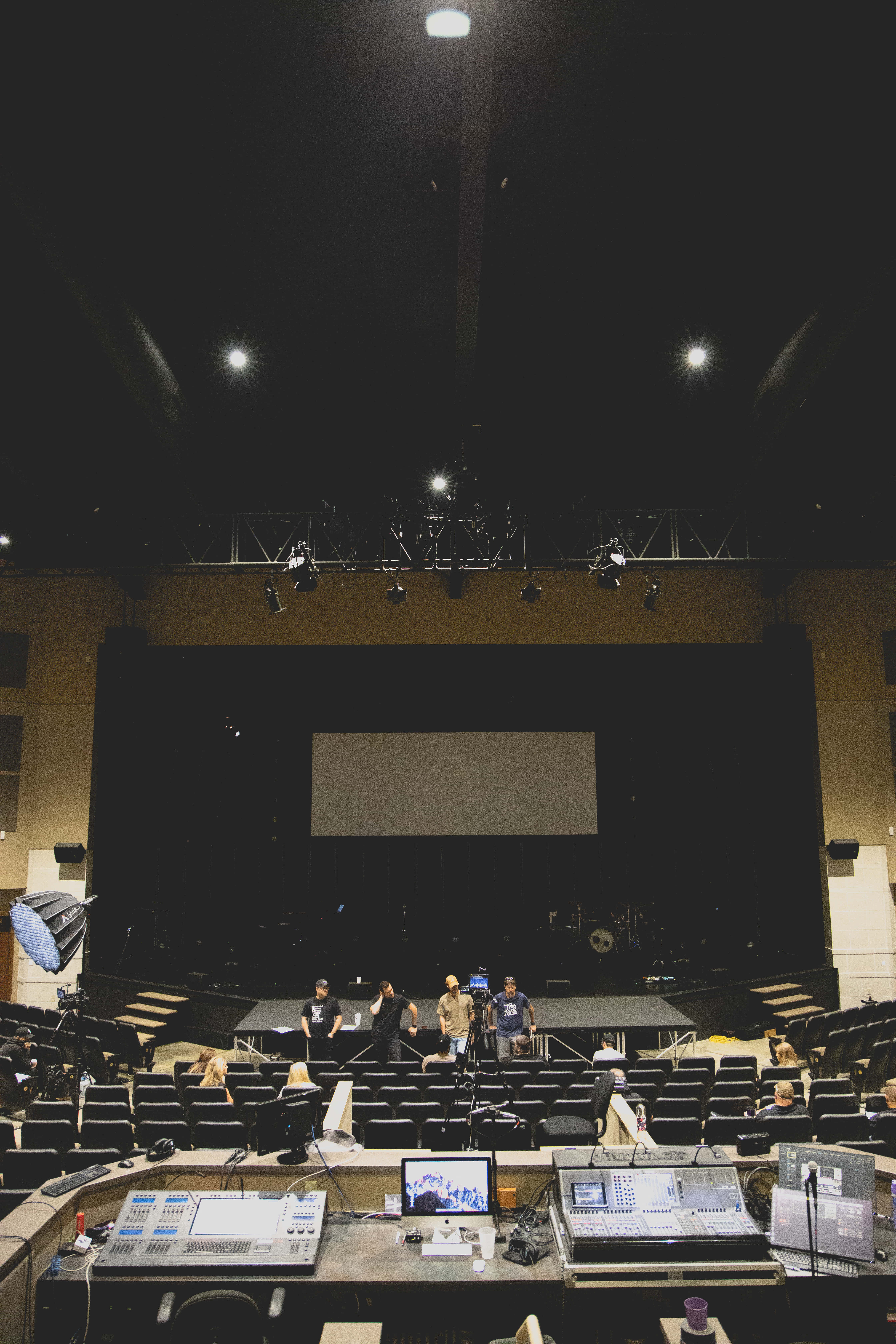 Church Stage 桌布 壁紙 — 燈光昏暗的劇院舞台上，工作人員在明亮的聚光燈下設置設備。