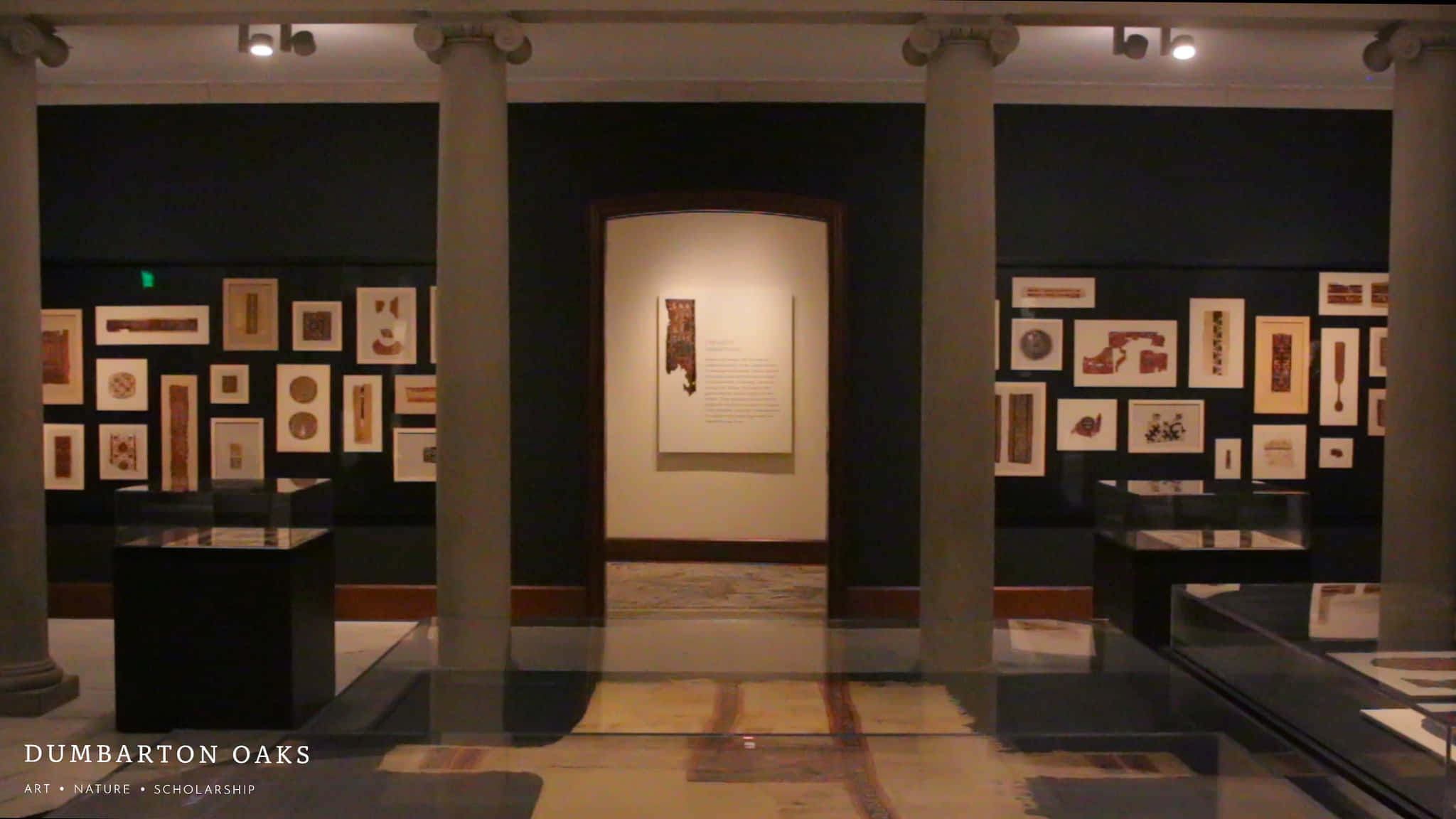 Museum 桌布 壁紙 — 燈光昏暗的博物館畫廊，擁有古典柱廊，在聚光燈下展示裝框的文物和玻璃陳列櫃。