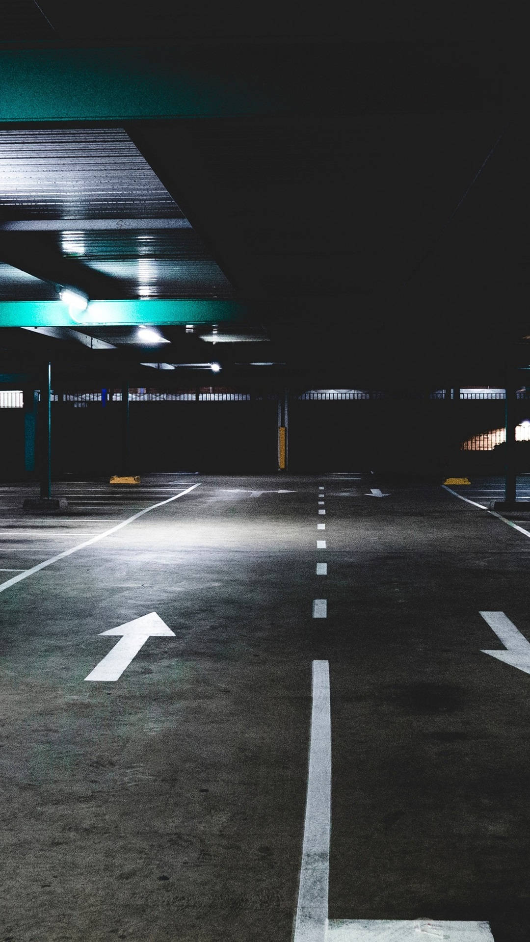 箭頭 桌布 壁紙 — 燈光昏暗的地下停車場，帶有鮮明的白色方向箭頭和發出綠色光芒的天花板燈，投下長長的影子。