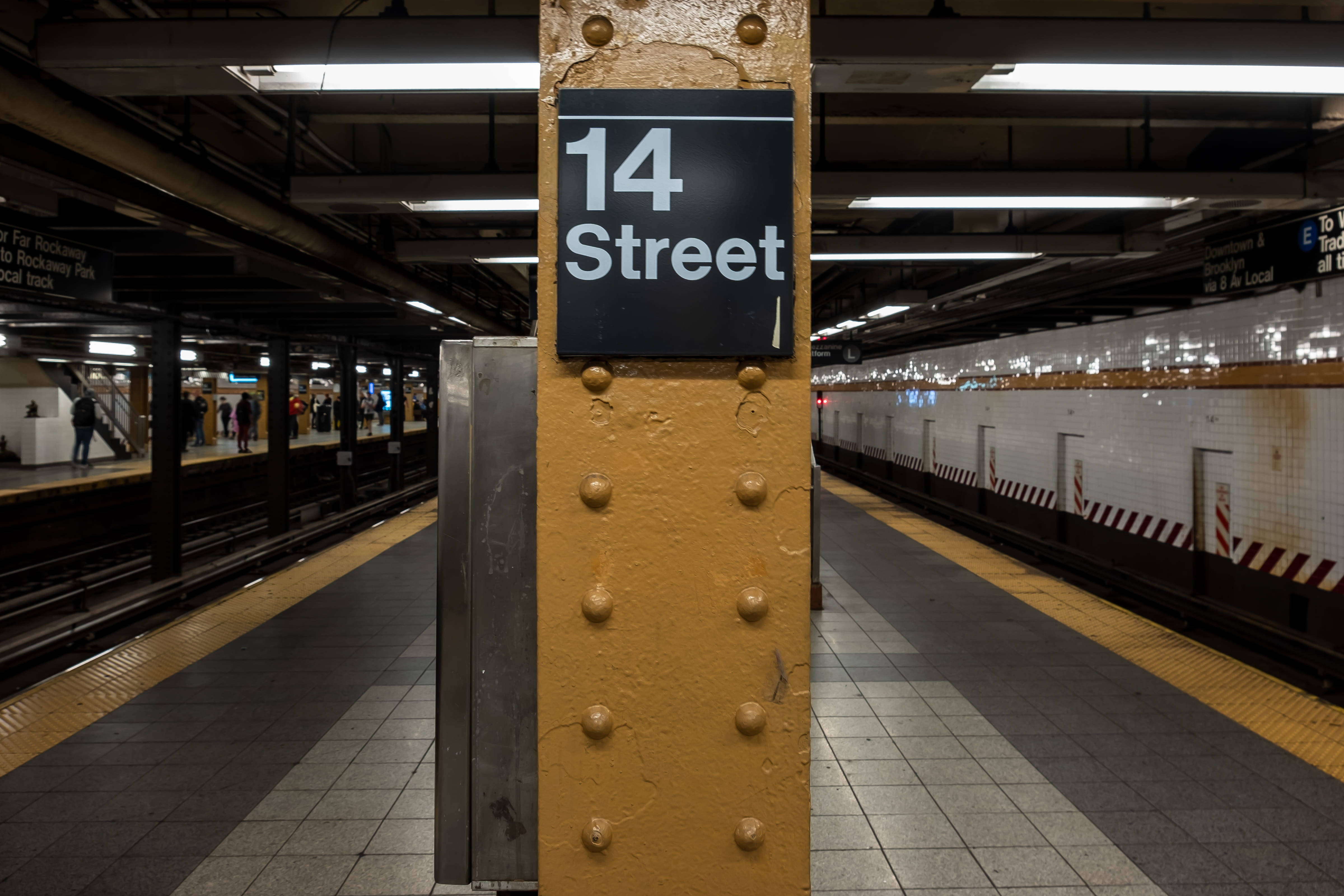 Subway 桌布 壁紙 — 燈光昏暗的地鐵站，一根風化的黃色柱子帶有「14 Street」標誌，兩側是瓷磚月台和遠處的通勤者。