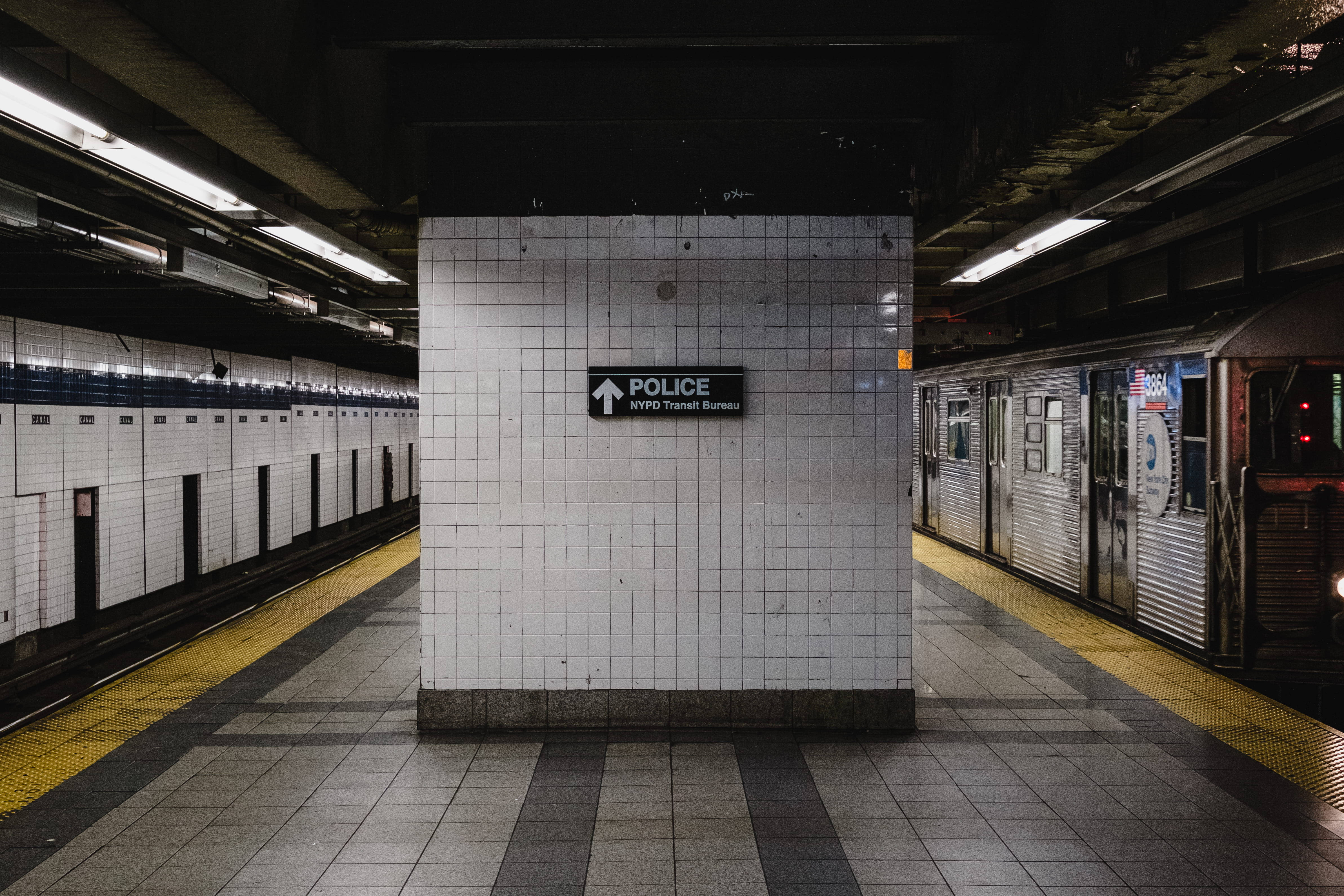 Subway 桌布 壁紙 — 燈光昏暗的地鐵站，白色瓷磚牆壁，警察標誌和月台上的列車。