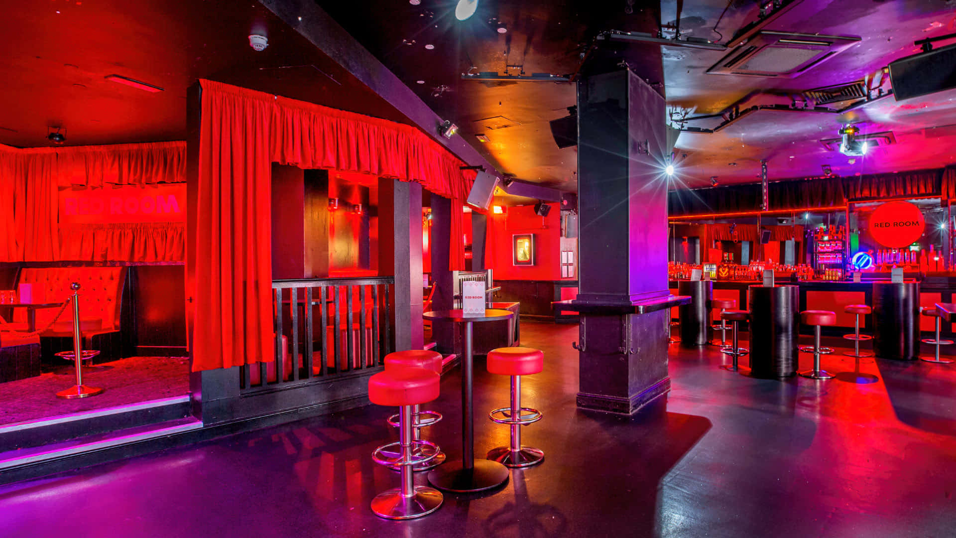 Red Room 桌布 壁紙 — 燈光昏暗的夜總會，沐浴在紅色和紫色的霓虹燈光中，設有高腳凳和舞台區域。