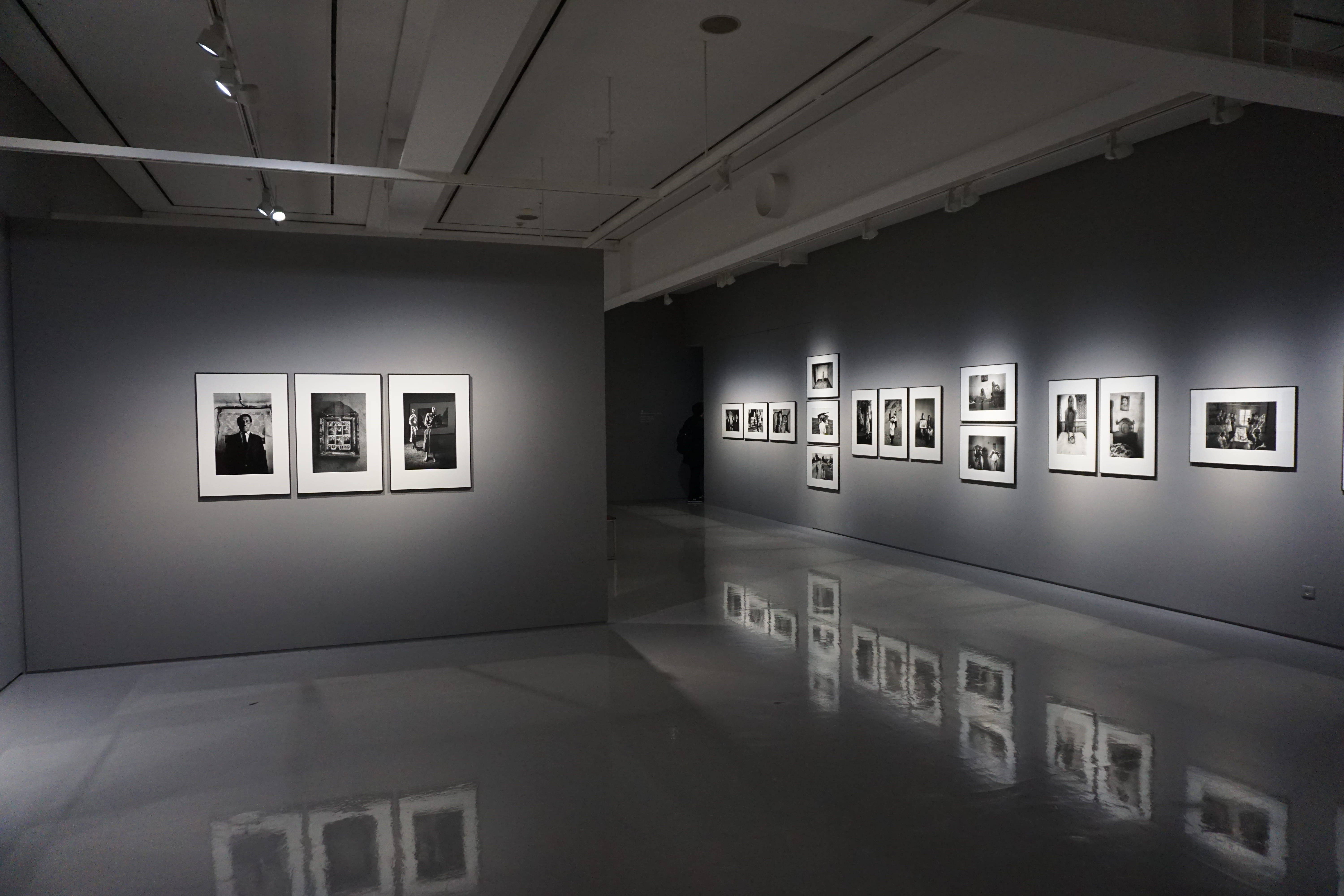 Gallery 桌布 壁紙 — 燈光昏暗的現代畫廊，灰色牆壁上掛著黑白裱框照片，映照在拋光地板上。
