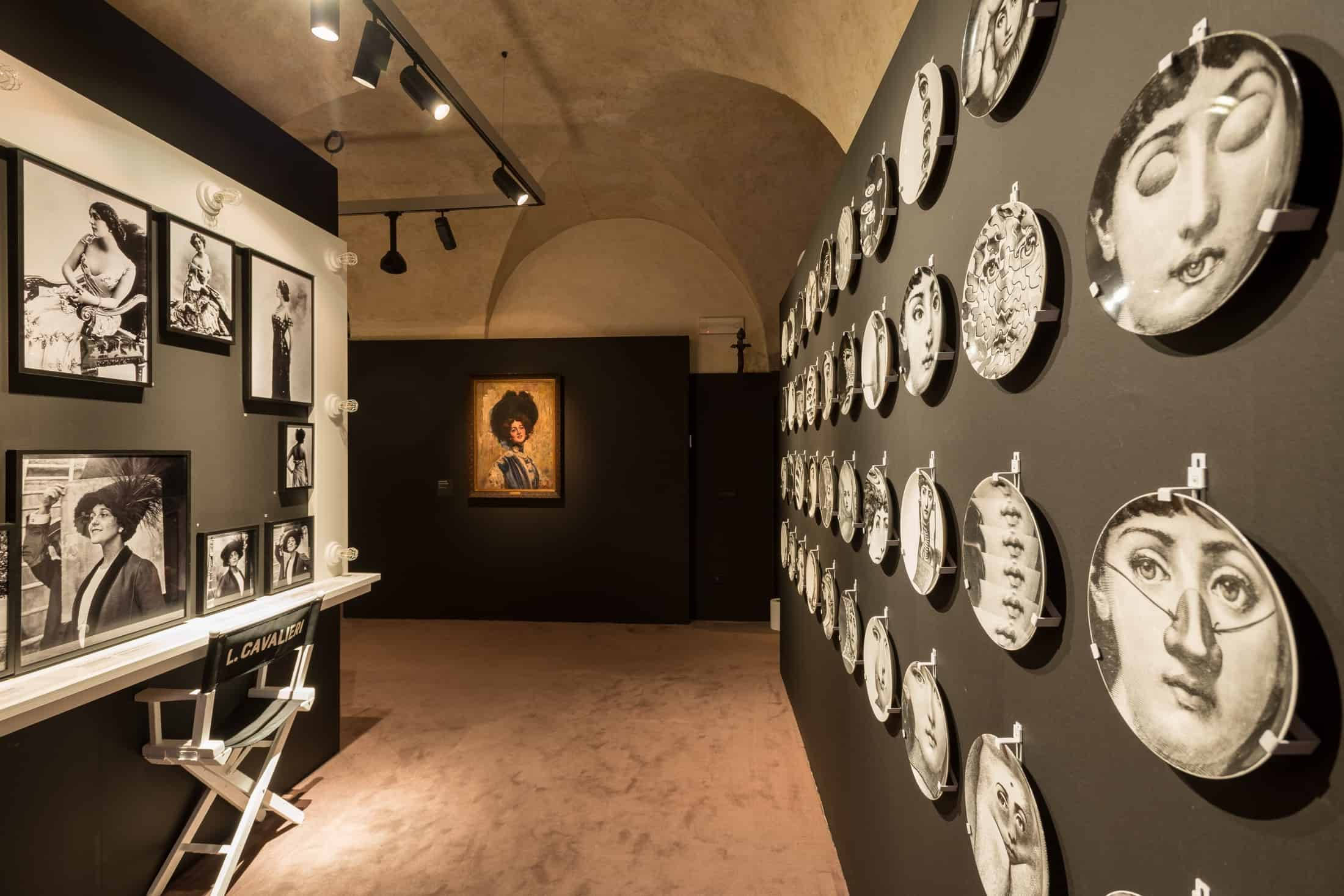 Ferragamo 桌布 壁紙 — 燈光昏暗的畫廊走廊，黑色牆壁展示著裱框的黑白肖像和圓形臉部藝術品，置於聚光燈下。