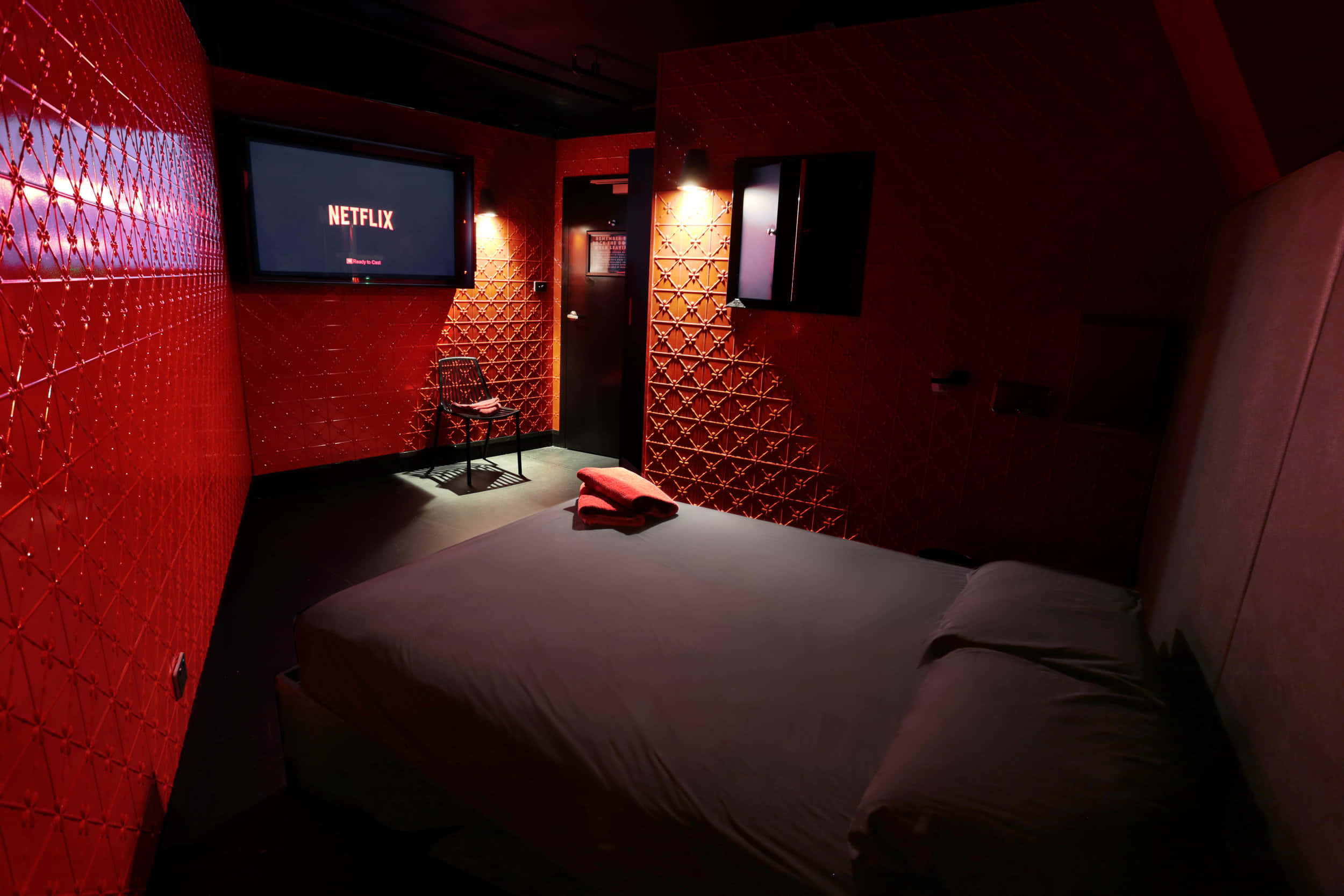 Red Room 桌布 壁紙 — 燈光昏暗的臥室，紅色紋理牆壁，床在顯示Netflix的電視下方。
