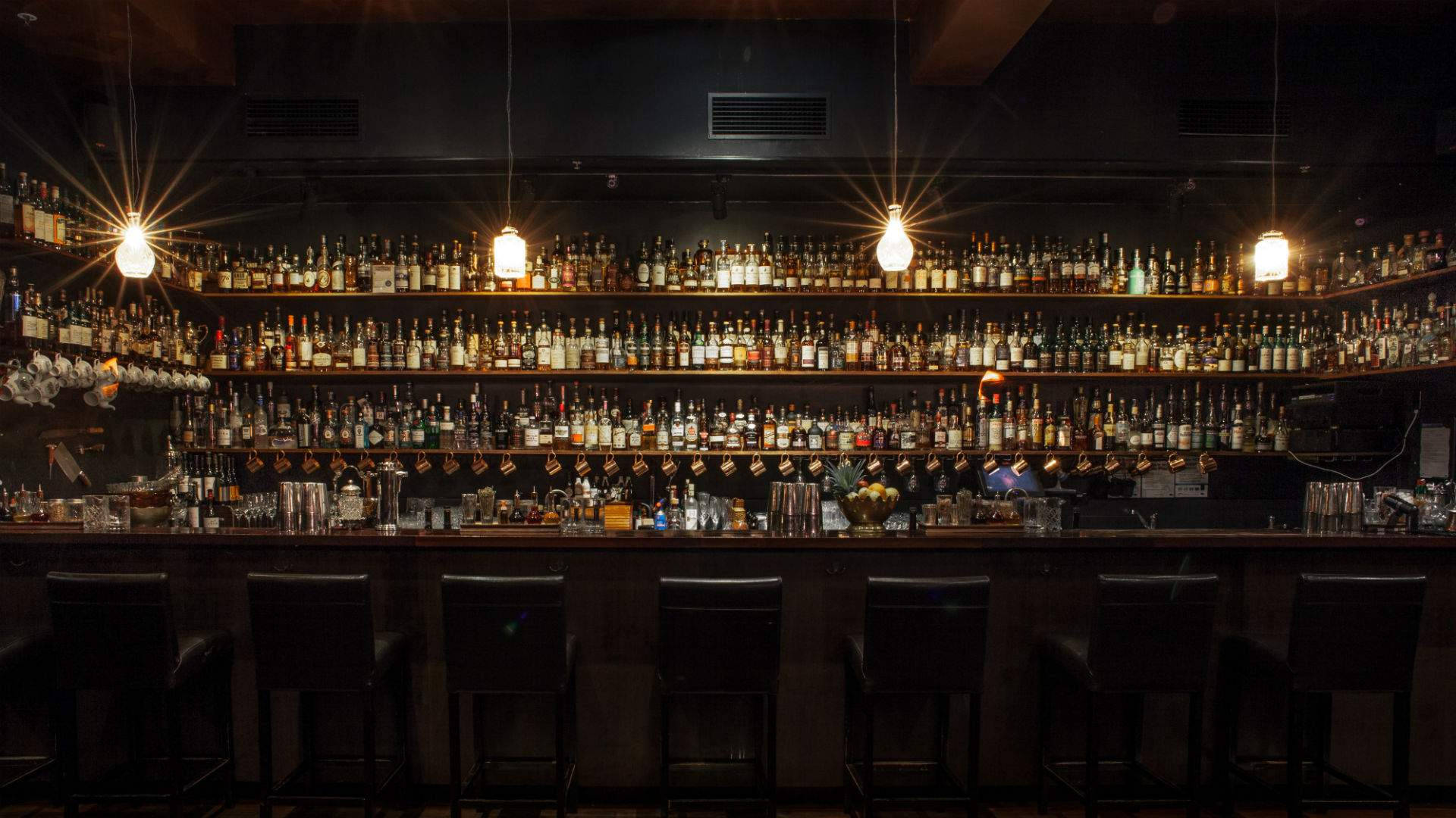 Melbourne 桌布 壁紙 — 燈光昏暗的酒吧，發光的吊燈照亮一排排的酒瓶和空凳子。