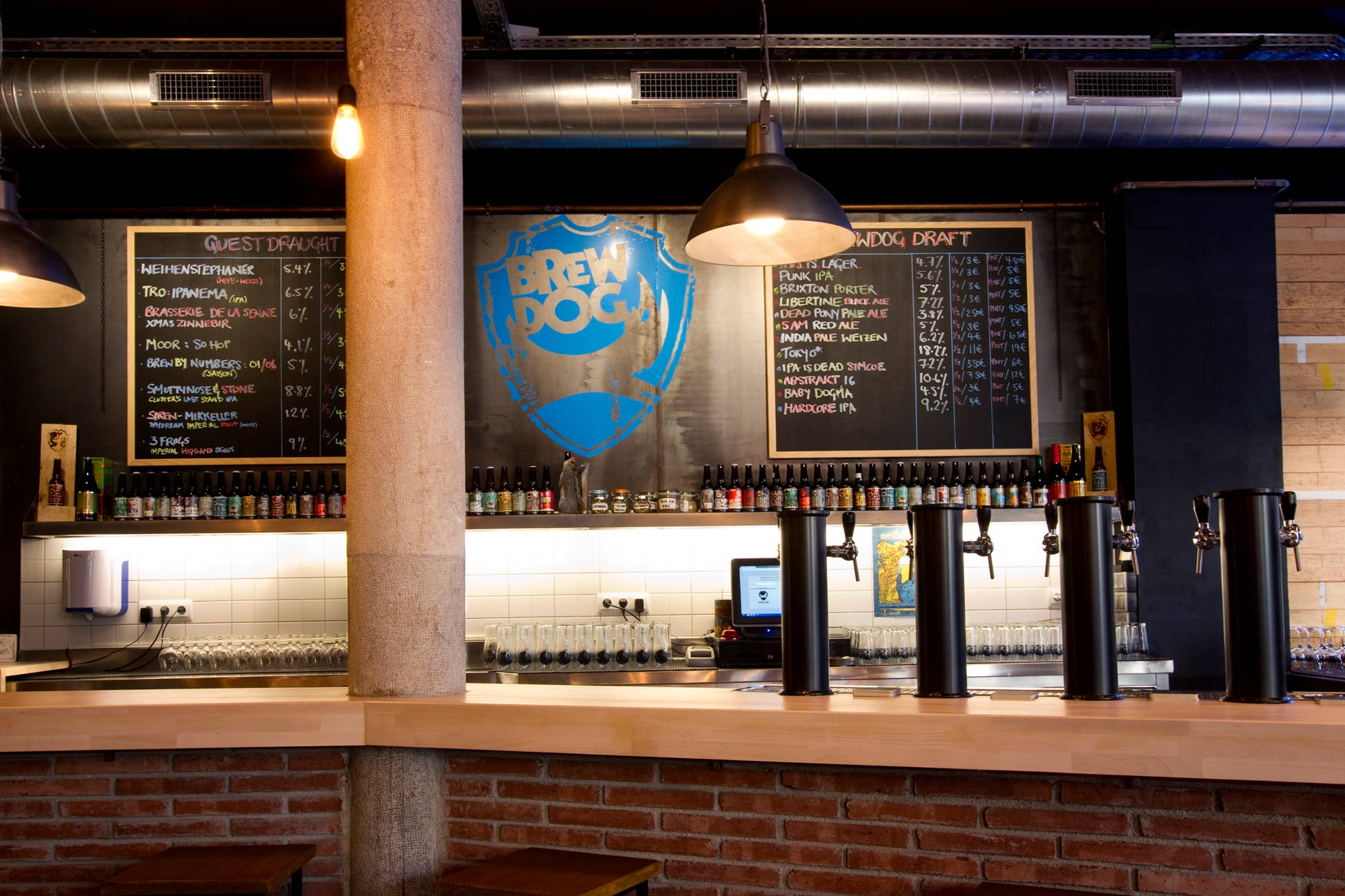 Drink 桌布 壁紙 — 燈光溫暖的BrewDog酒吧，有裸露磚牆、黑板菜單和掛在吊燈下的啤酒龍頭。
