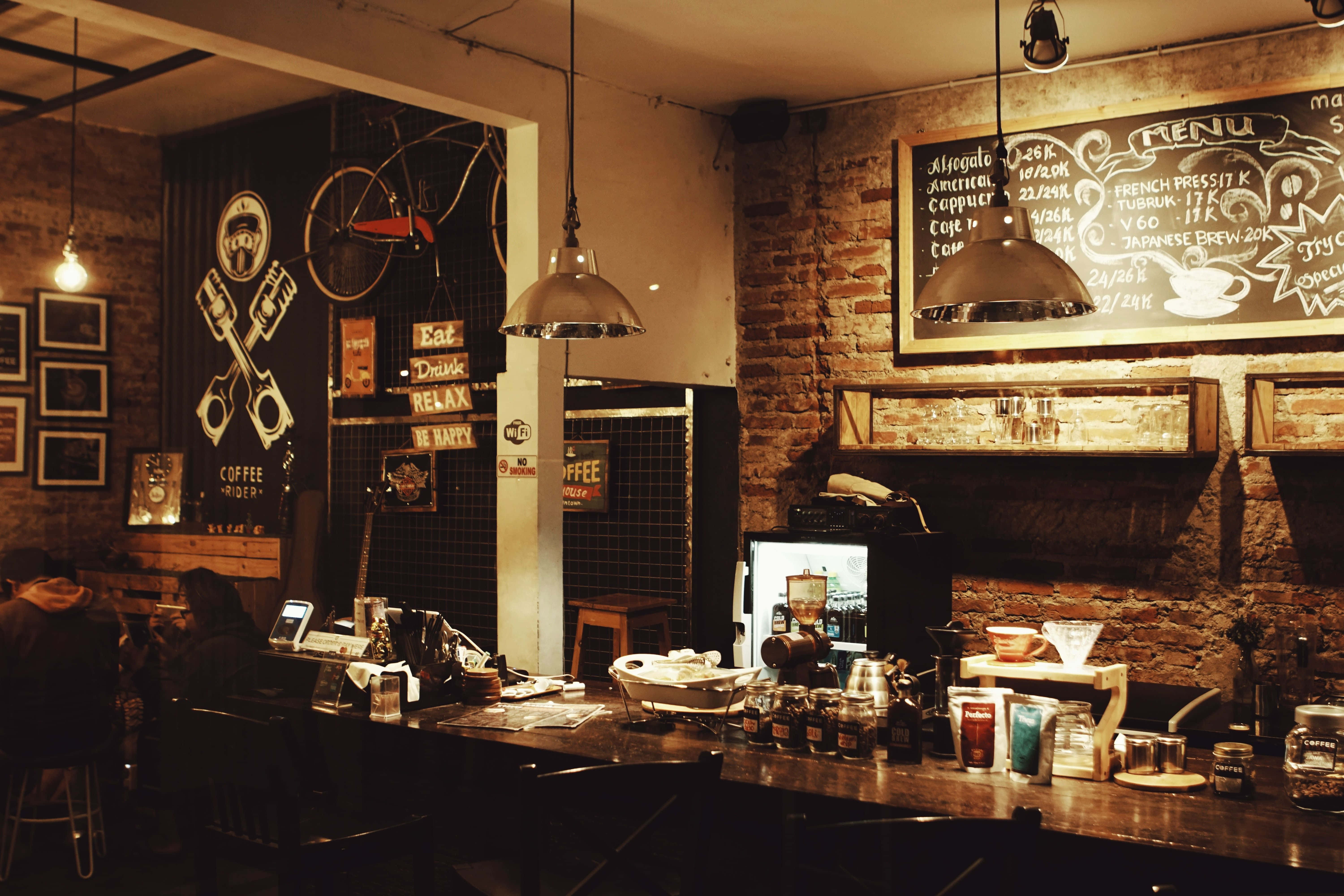 Cozy 桌布 壁紙 — 燈光溫暖的鄉村風格咖啡店，裸露磚牆、黑板菜單掛在木製櫃檯上方，復古吊燈散發出舒適的光芒。