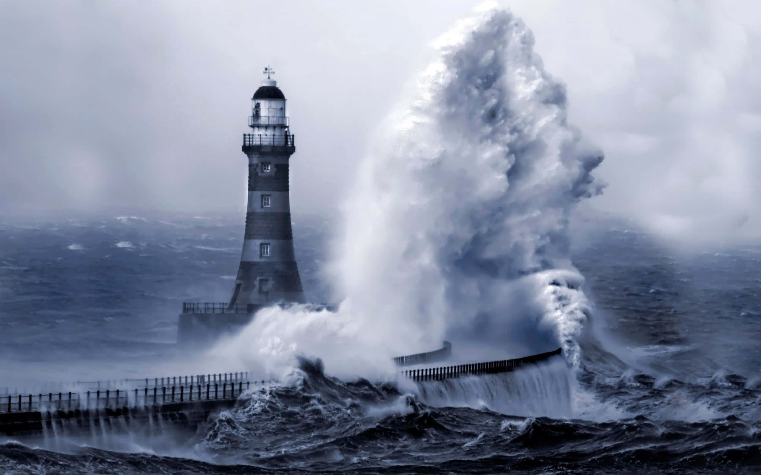 Lighthouse 桌布 壁紙 — 燈塔在灰暗的天空下，傲然挺立於洶湧的暴風海浪之中。