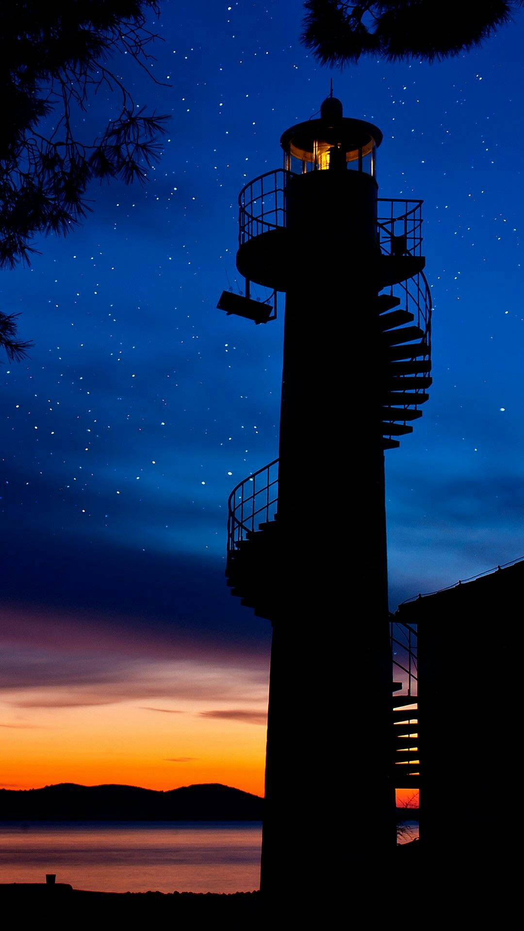 夜空 桌布 壁紙 — 燈塔的剪影聳立在繁星點點的暮色天空中，下方是橙色的地平線和寧靜的大海。