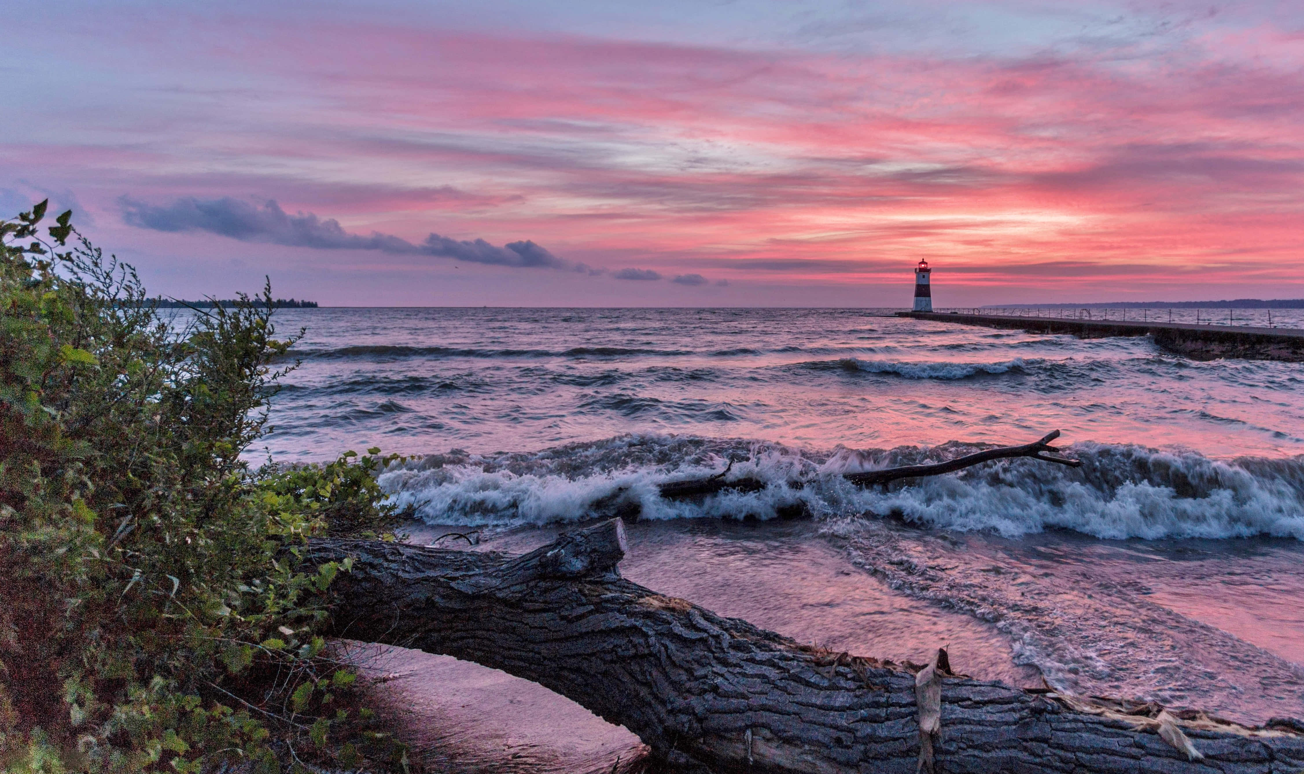 Lake Erie 桌布 壁紙 — 燈塔矗立在碼頭盡頭，海浪拍打著倒下的原木，天空呈現出充滿活力的粉紅色和紫色日落。