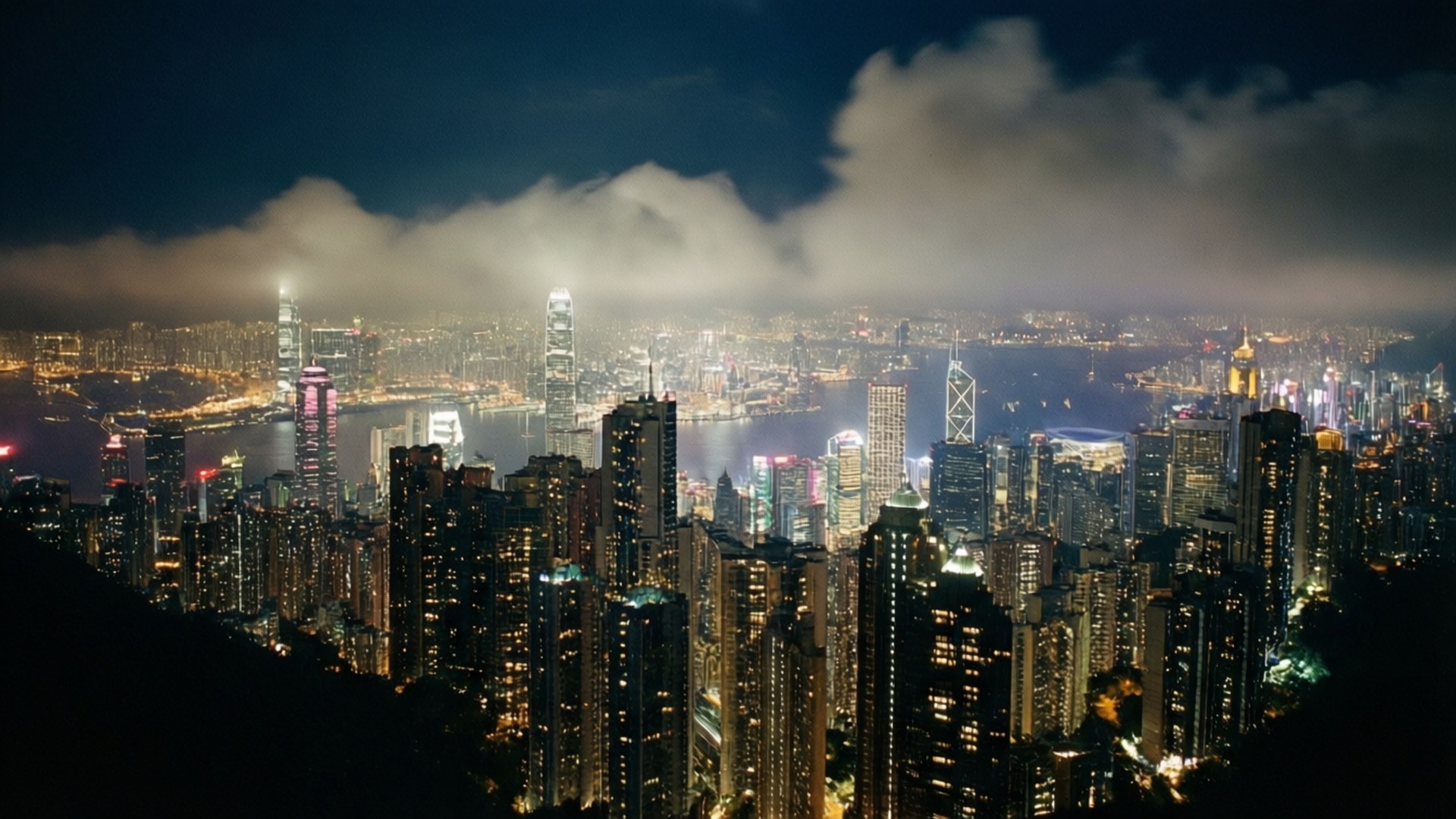 燈火之巔 壁紙 — 香港令人驚嘆的夜景，閃爍的摩天大樓和霧氣瀰漫的港口，天空多雲。
