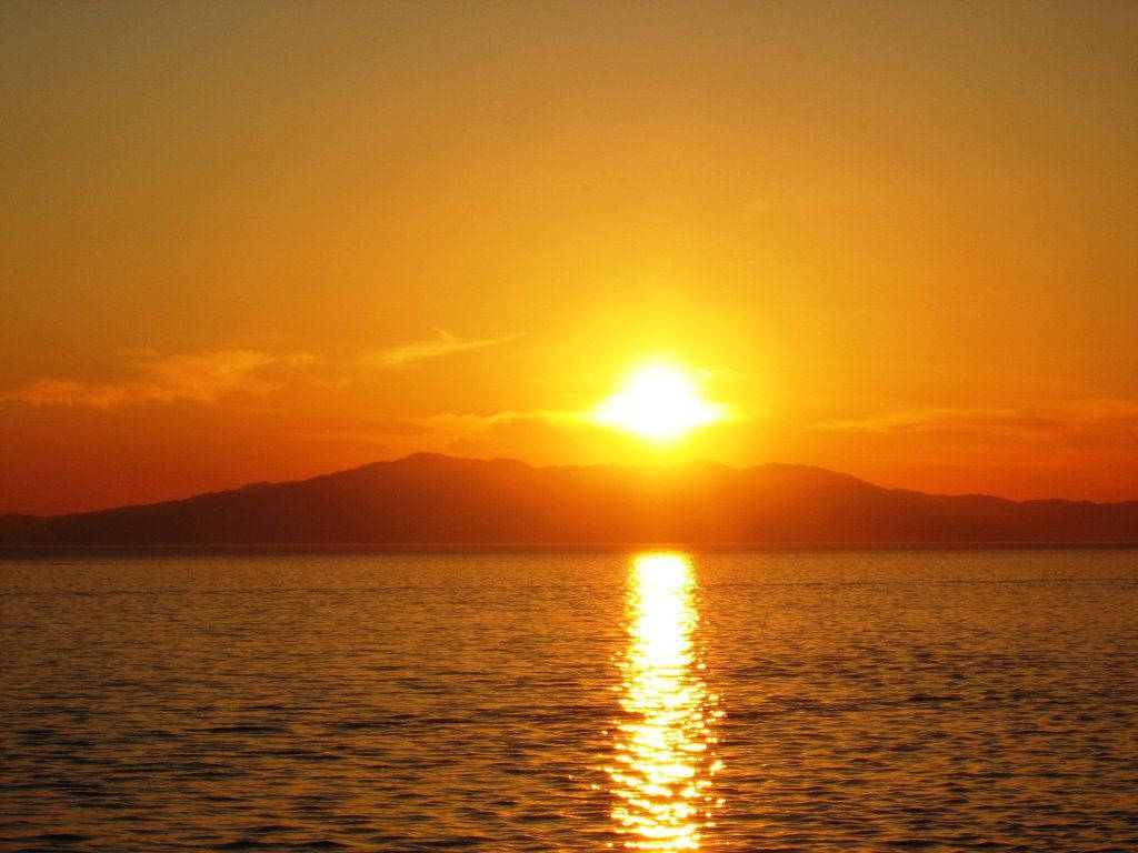 旭日東昇 桌布 壁紙 — 燦爛的夕陽在平靜的水面上灑下金色光芒，遠山在發光的地平線上形成剪影。