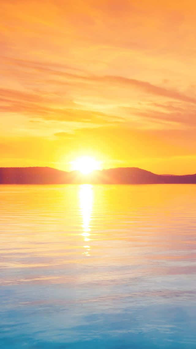 Sunrise iPhone 桌布 壁紙 — 燦爛的夕陽在平靜的湖面上灑下金色的光芒，遠山在發光的天空下形成剪影。