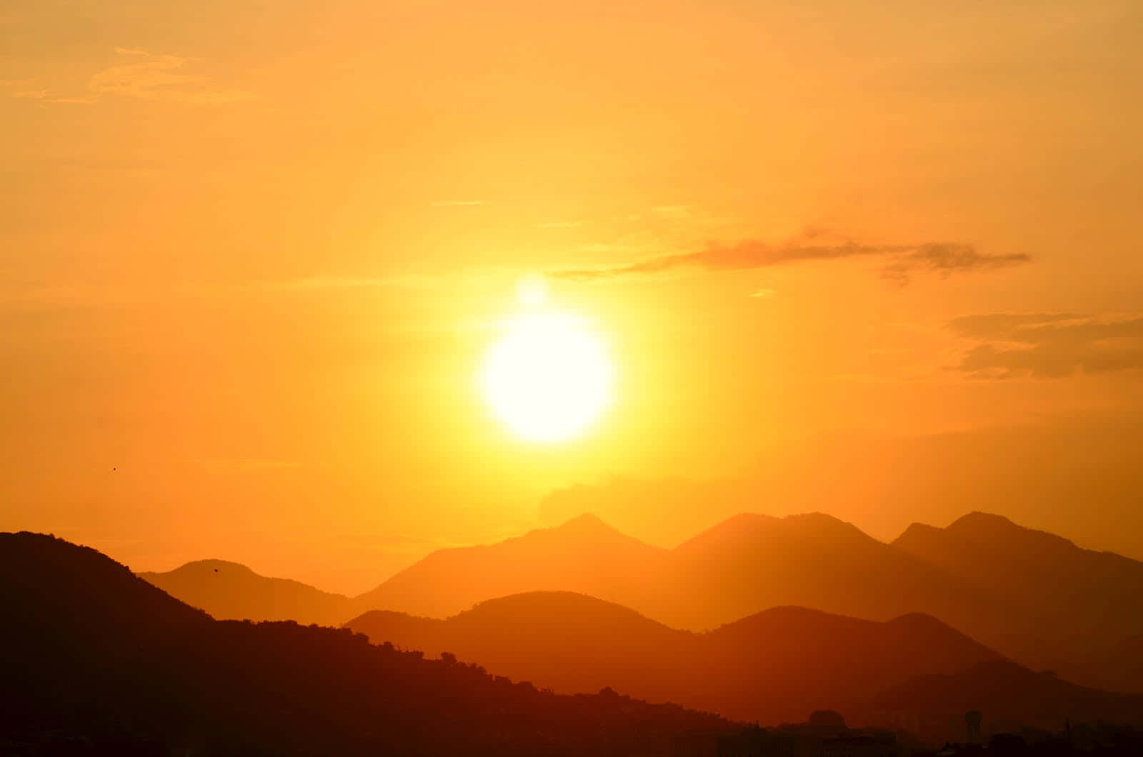 Cute Sunset 桌布 壁紙 — 燦爛的太陽在層層疊疊的山巒剪影後落下，在天空中投射出溫暖的橙色和金色色調。