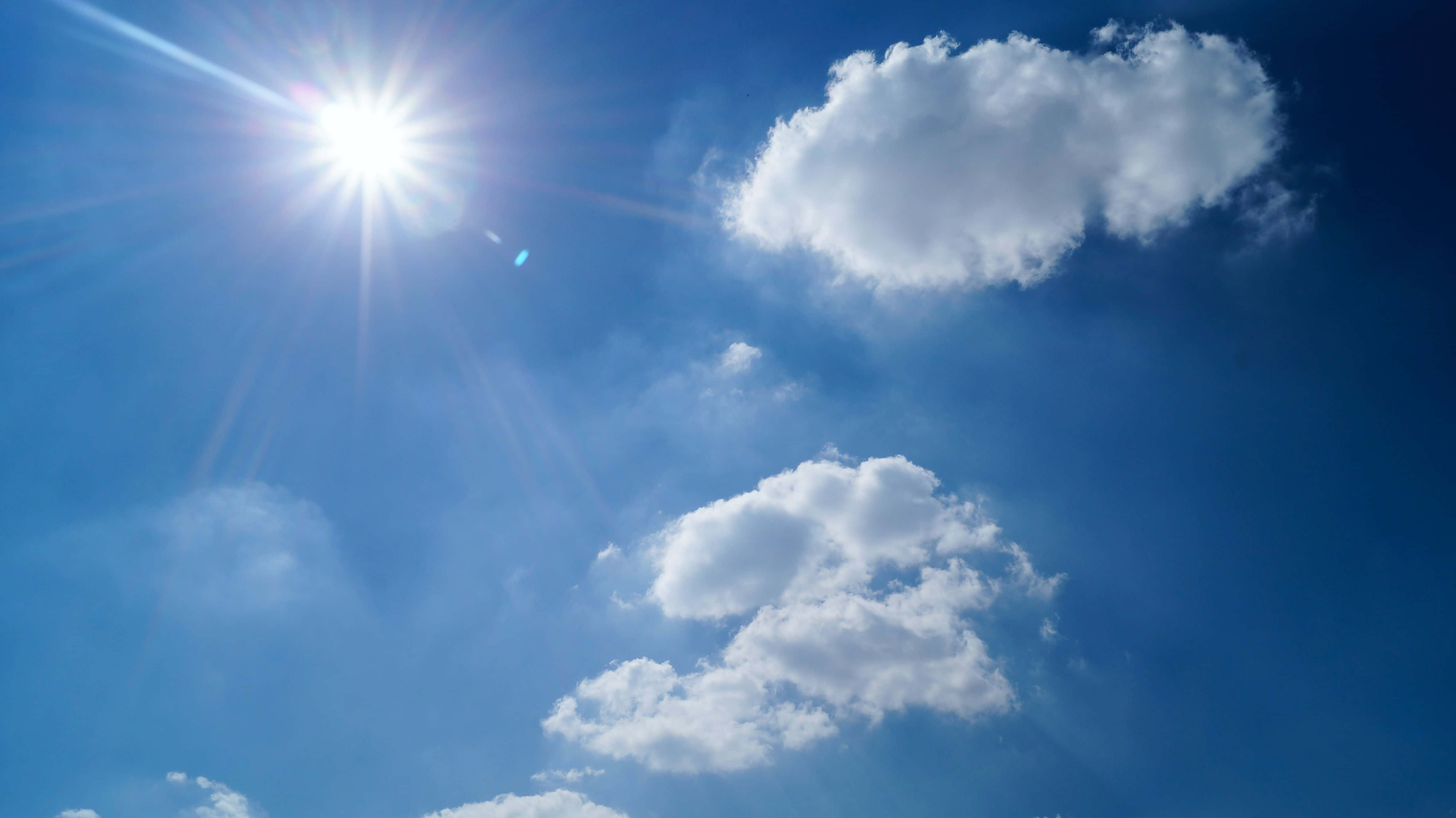 sunny 桌布 壁紙 — 燦爛的太陽在點綴著蓬鬆白雲的鮮豔藍天上放射出明亮的光芒。