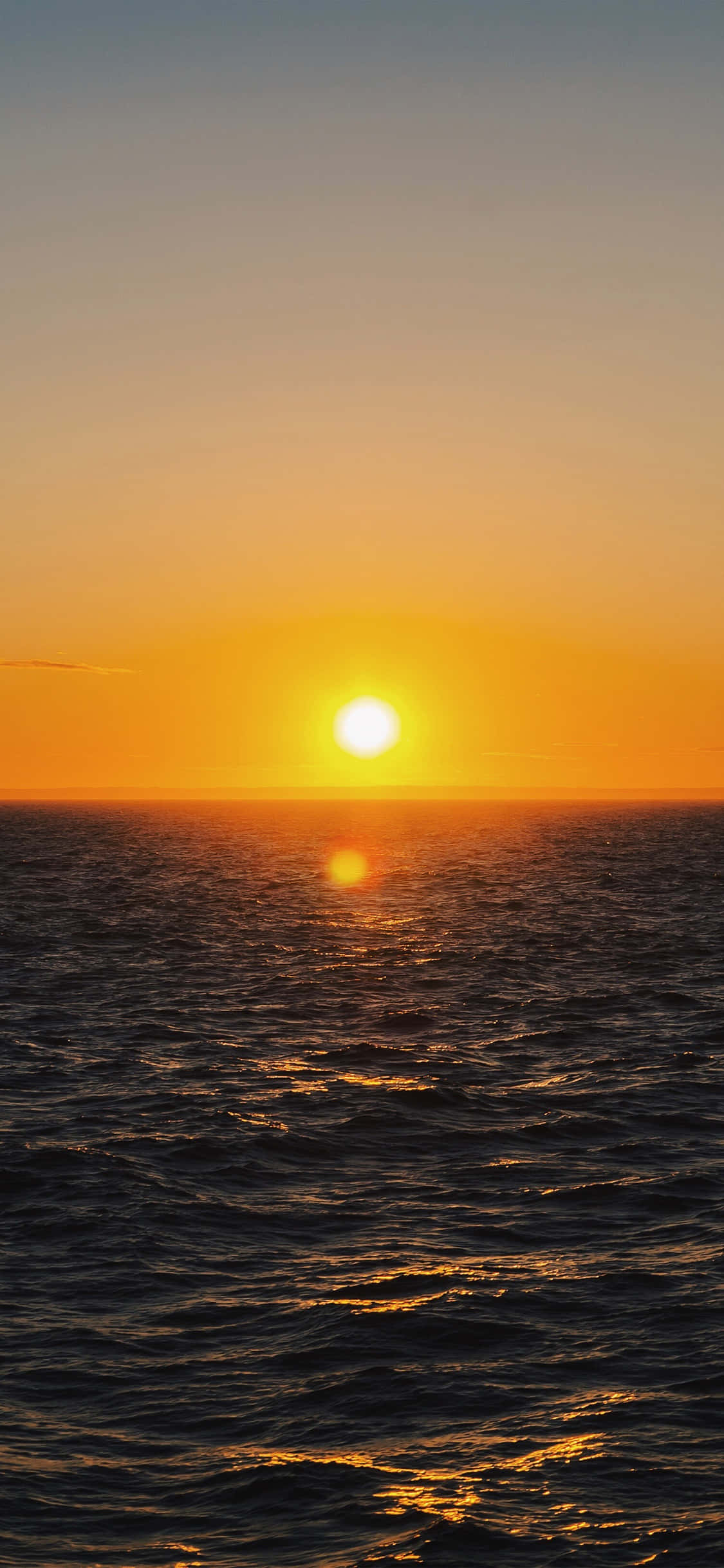 Sunrise iPhone 桌布 壁紙 — 燦爛的太陽沉入地平線下，在漸變天空下，在廣闊的波濤洶湧的海洋上投下金色的倒影。
