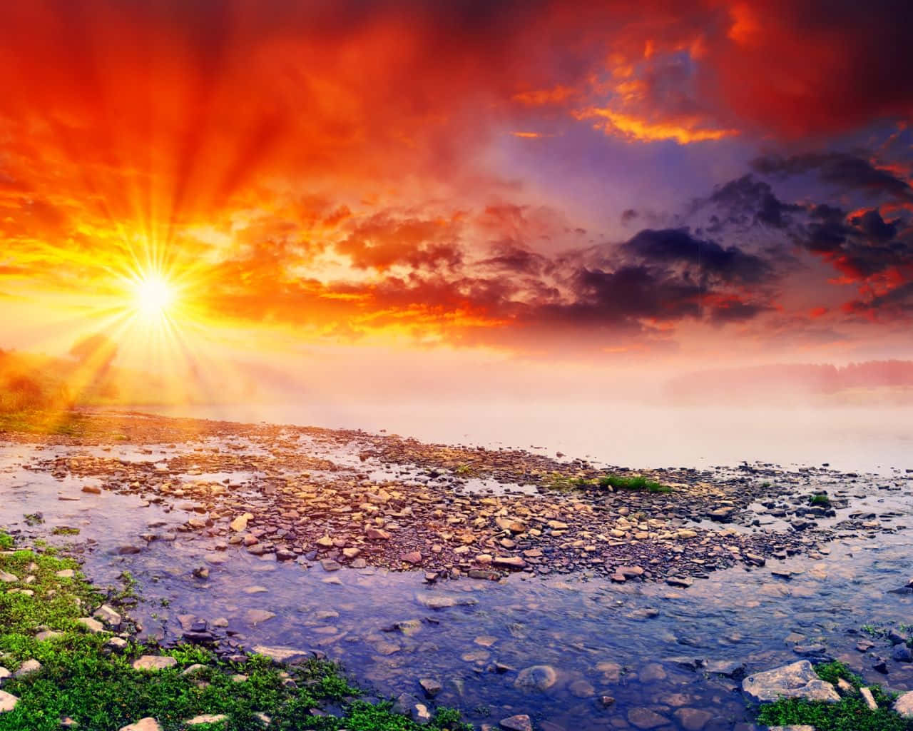 Spring Sunset 桌布 壁紙 — 燦爛的日出穿過火紅的橙色雲層，照耀在霧氣籠罩的河床上，河床佈滿濕石和綠色苔蘚。