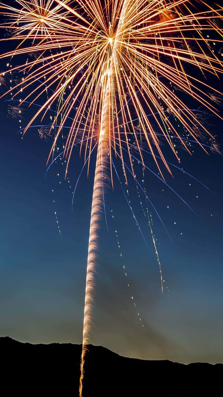 Fireworks 桌布 壁紙 — 燦爛的金色煙火在黑暗的夜空中，於剪影般的山丘上方爆炸，留下火花和藍色條紋。