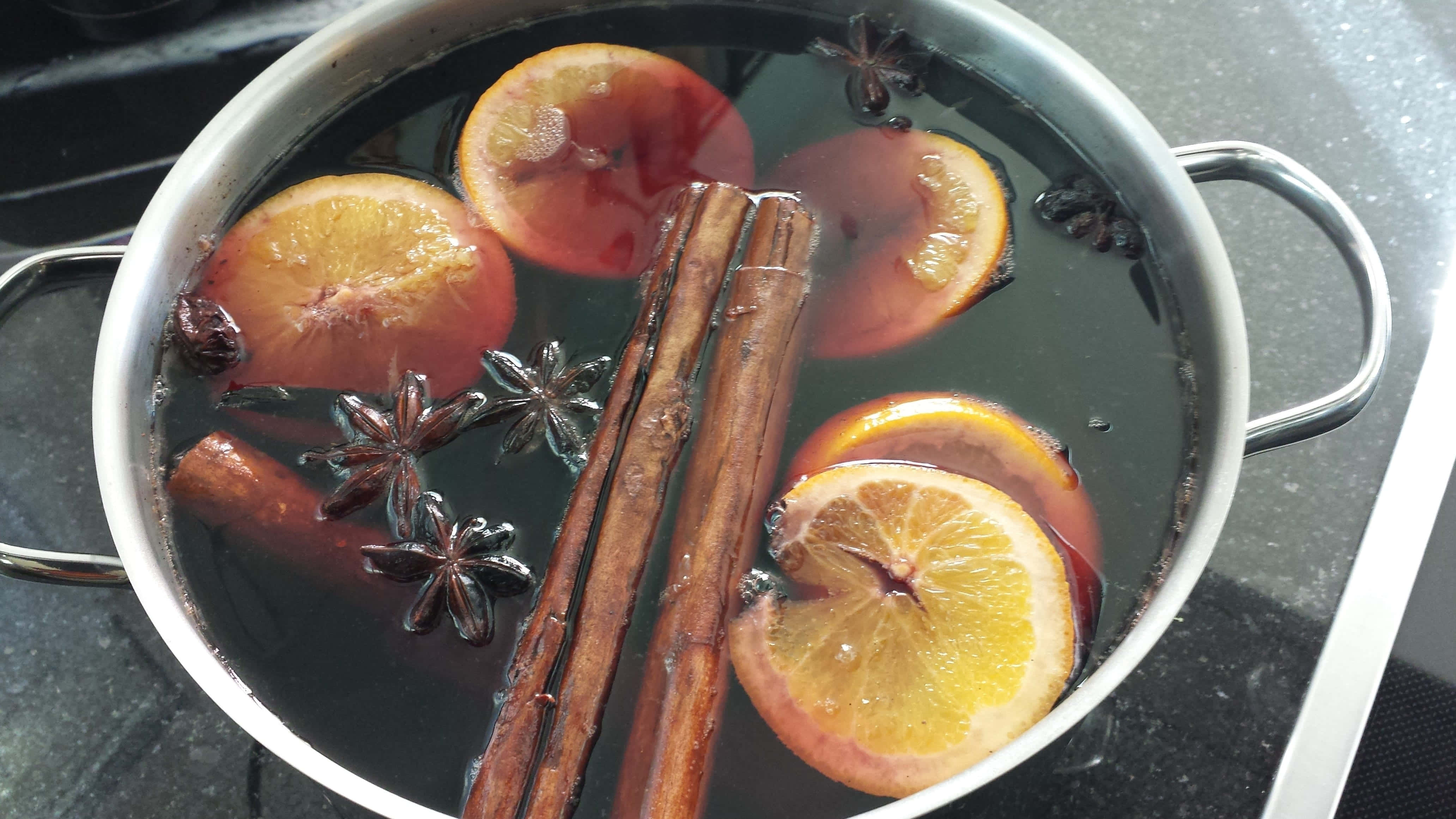 Mulled Wine 桌布 壁紙 — 爐上一個銀色鍋子盛載著深色香料熱紅酒，浮有橙片、肉桂棒和八角。