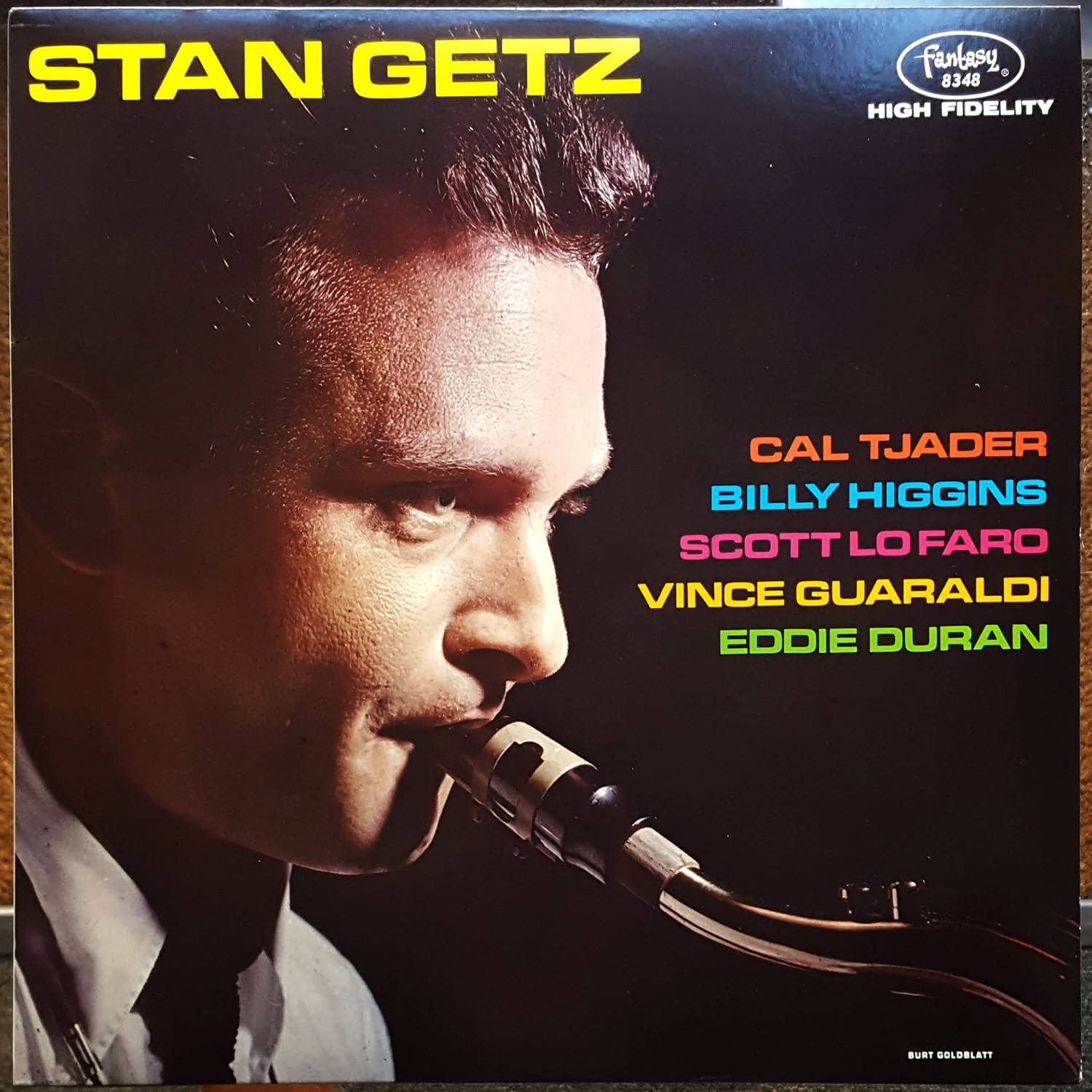 音樂 桌布 壁紙 — 爵士薩克斯風手 Stan Getz 的側面特寫，在深色背景上帶有彩色文字，對著復古麥克風演奏。