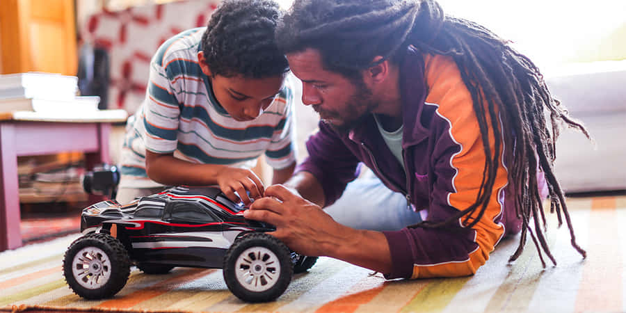Rc Cars 桌布 壁紙 — 父親和兒子在室內的條紋地毯上專注地組裝一輛黑紅色的遙控車。